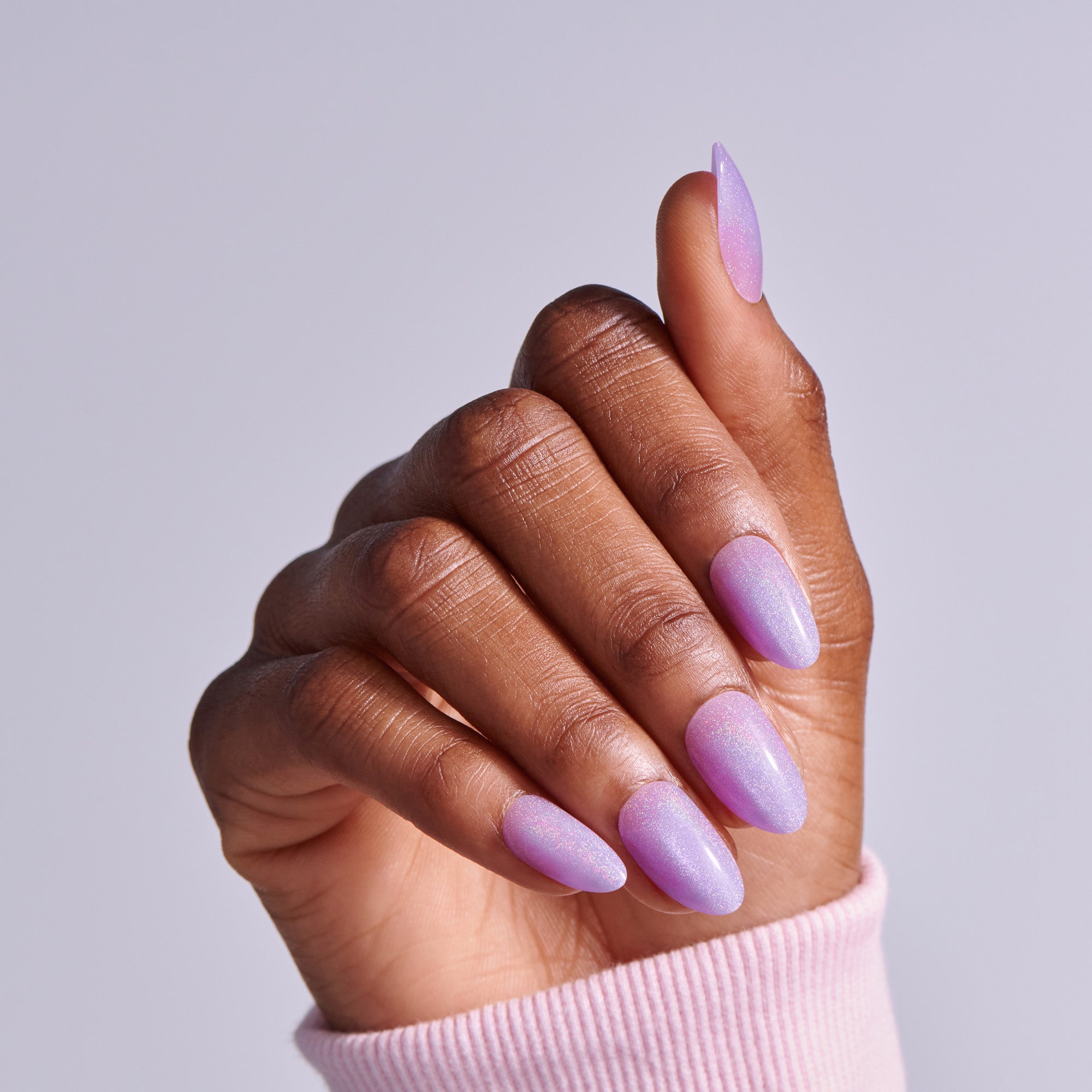 Hand displaying purple shimmer nail polish on almond-shaped nails against light background.
