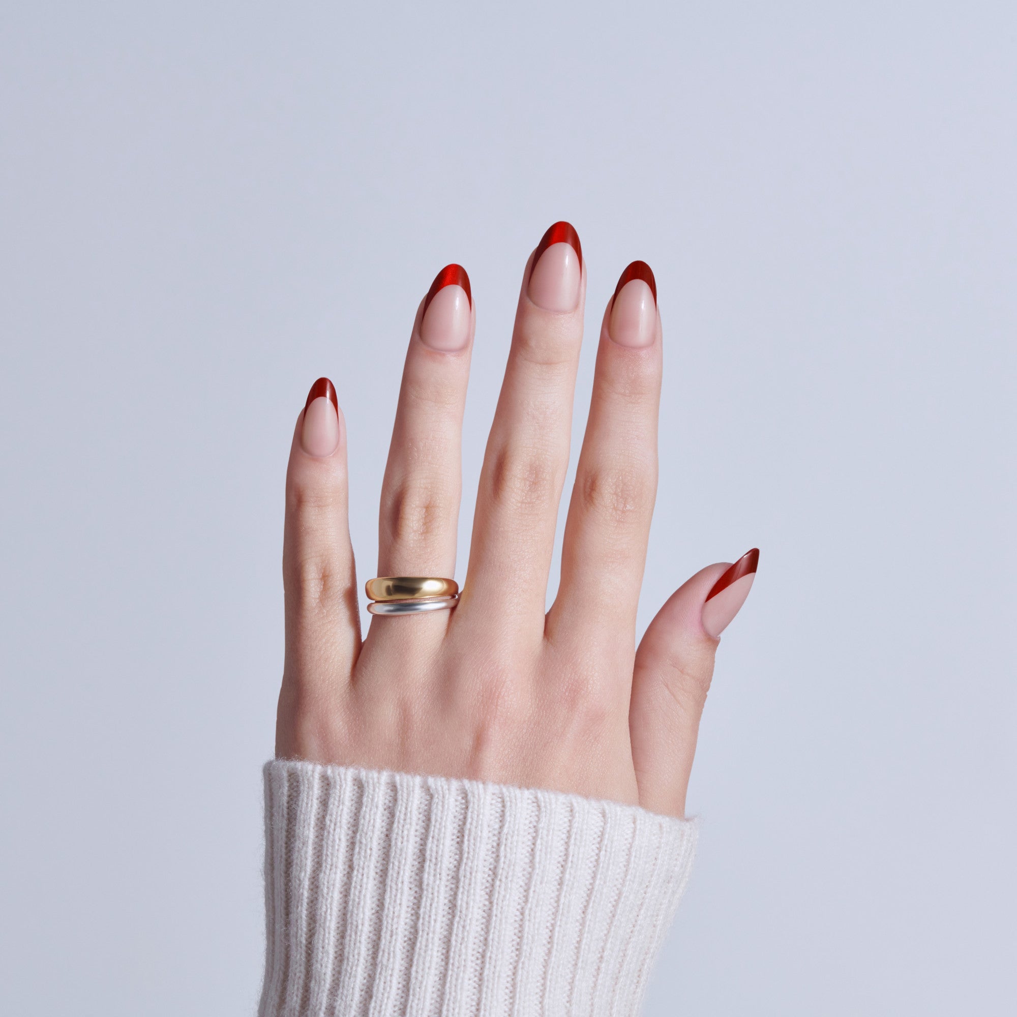 Hand with red and white French manicure nails wearing gold and silver rings.