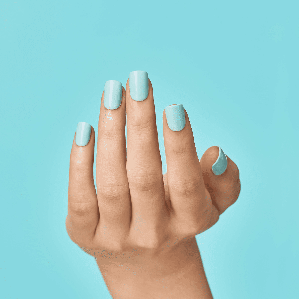 Hand with light mint green press-on nails against a matching mint green background, showing the ease of peeling off one nail for removal.