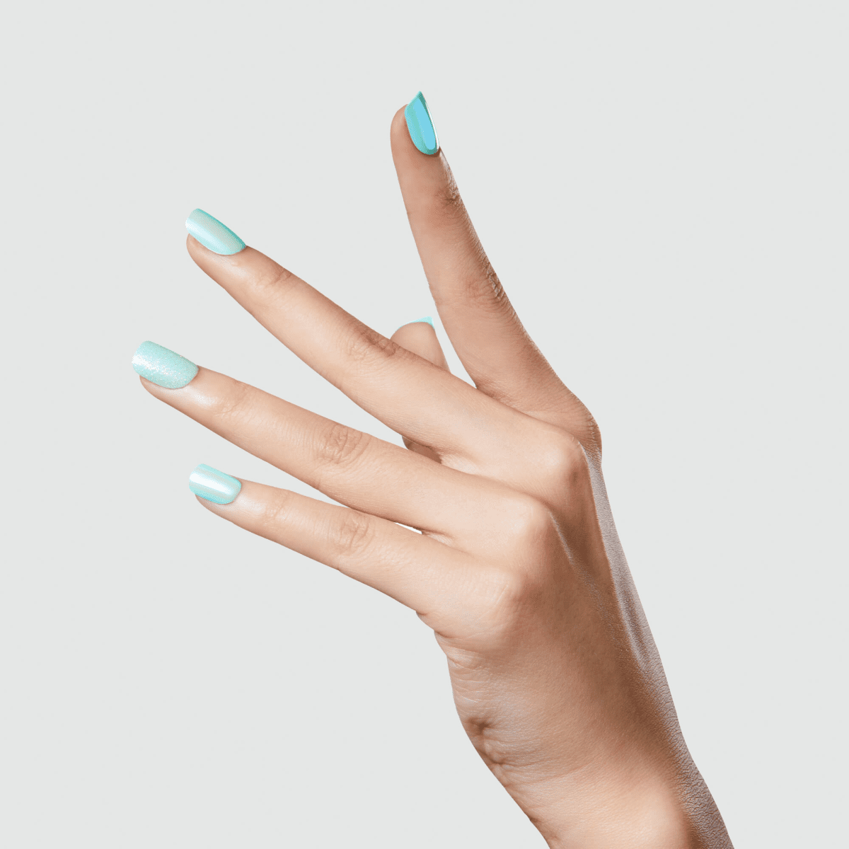 Hand with long nails wearing imPRESS Press-On Manicure in shades of light blue and aqua, featuring a matte and shimmer finish against a light gray background.