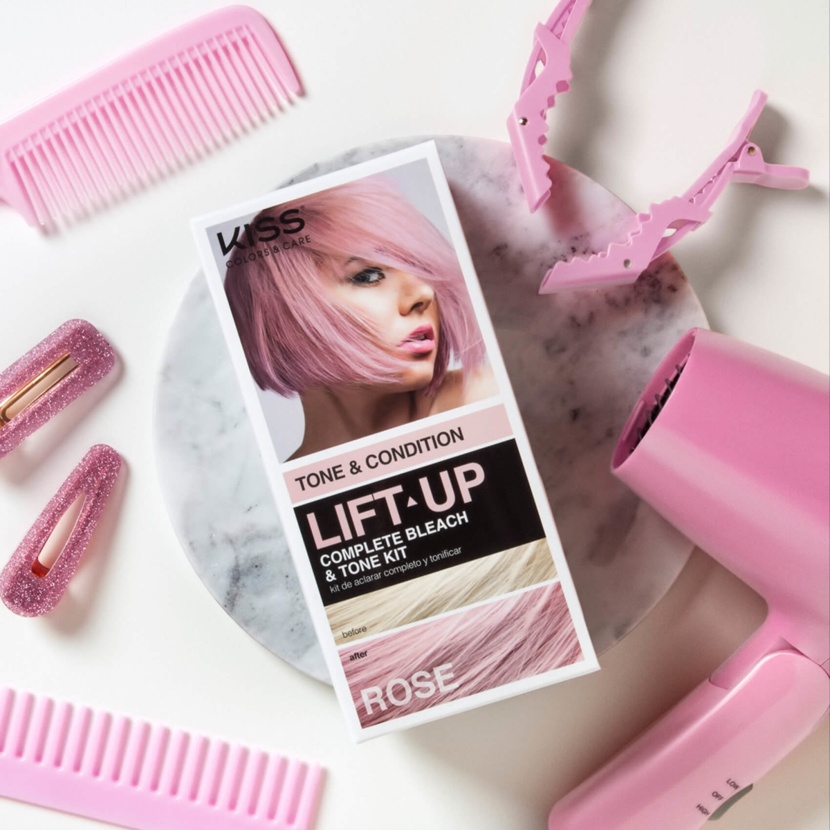 KISS Lift Up Complete Bleach & Tone Kit box with a woman’s pink bob hair on the front, surrounded by pink hair clips, combs, and a hair dryer on a white surface.