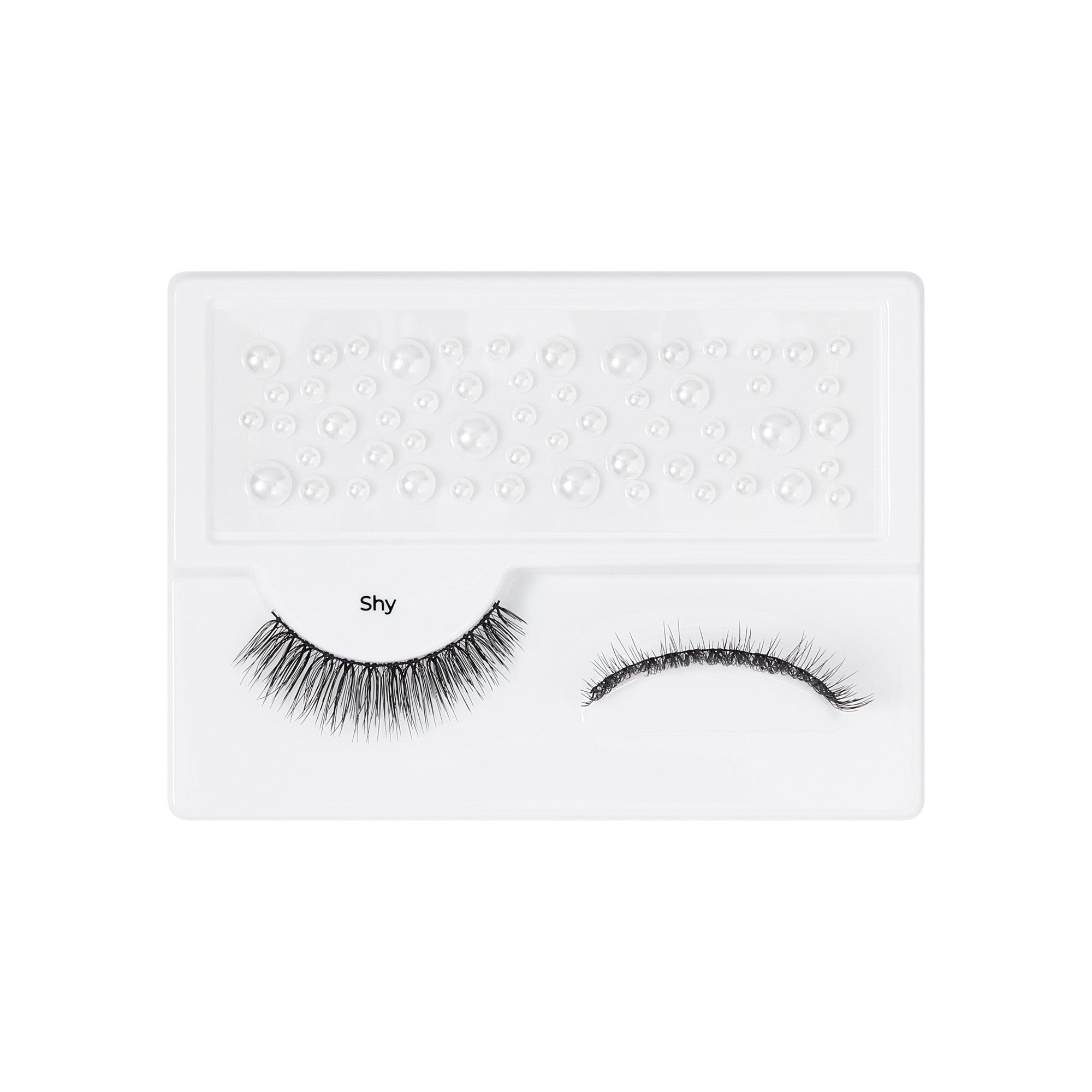 The image features a pair of false eyelashes displayed on a white tray. The lashes are labeled "Shy" and are arranged neatly, with one set appearing fuller and longer than the other. The tray has a textured surface with small, raised dots, likely designed to hold the lashes securely in place. The overall presentation is clean and minimalistic, emphasizing the eyelashes themselves.