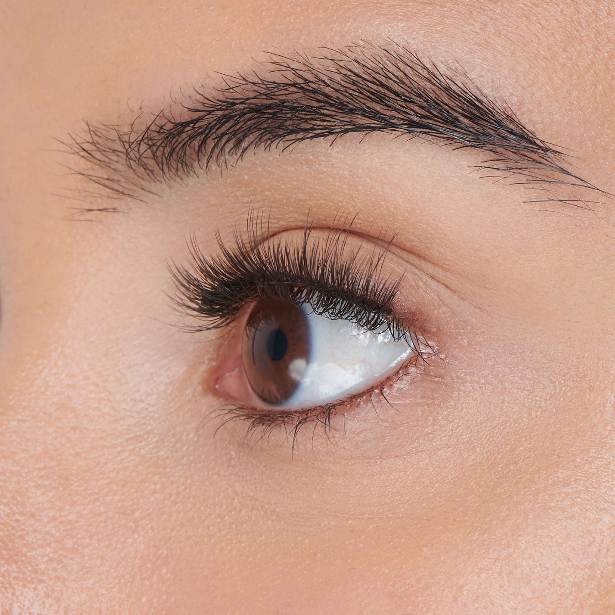 The image features a close-up of a human eye, showcasing the intricate details of the eyelashes and the skin around the eye. The eye has a warm brown iris, and the eyelashes appear long and well-defined. The skin surrounding the eye is smooth and has a natural tone, highlighting the eye&