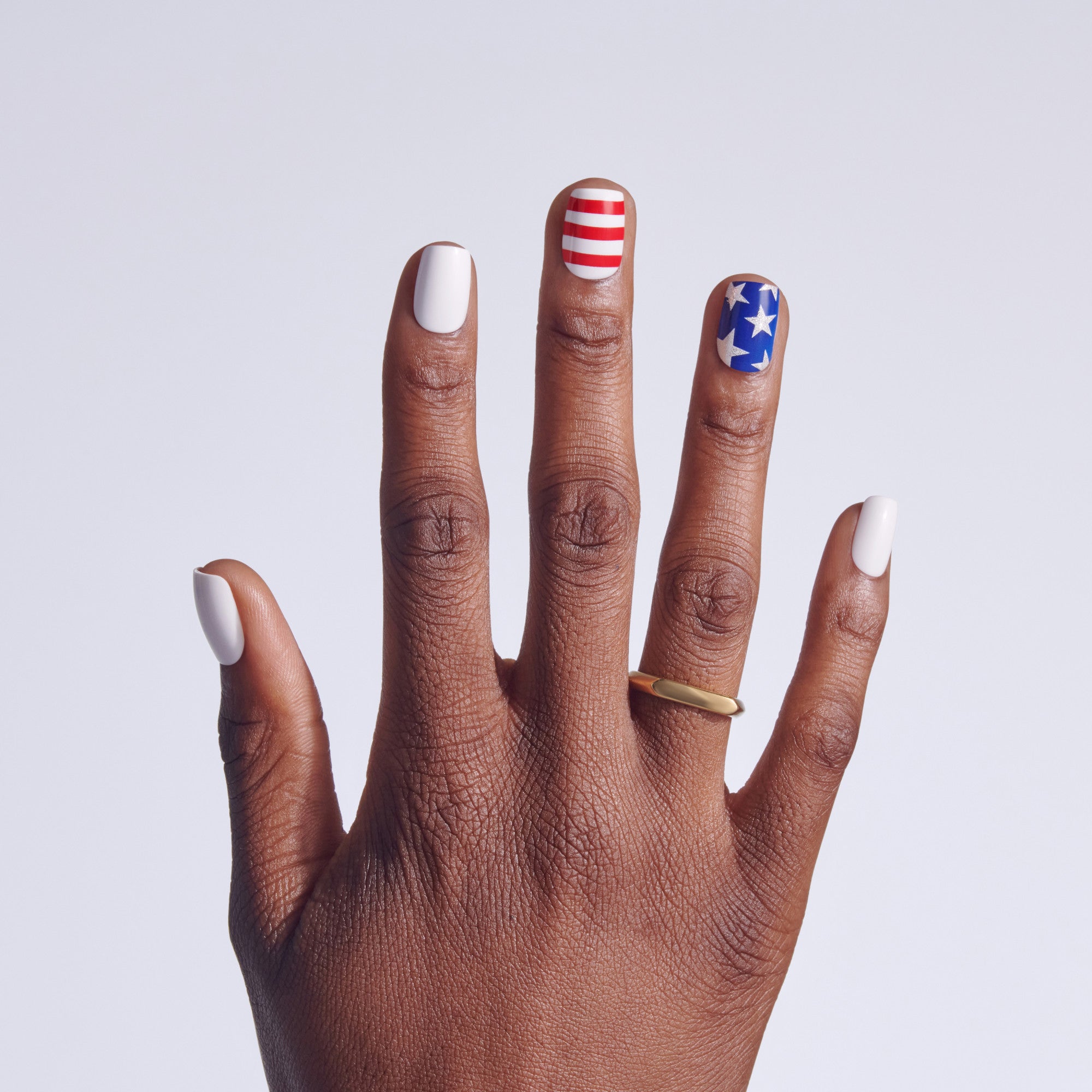 Hand with patriotic nail art: white, red/white stripes, blue with stars.