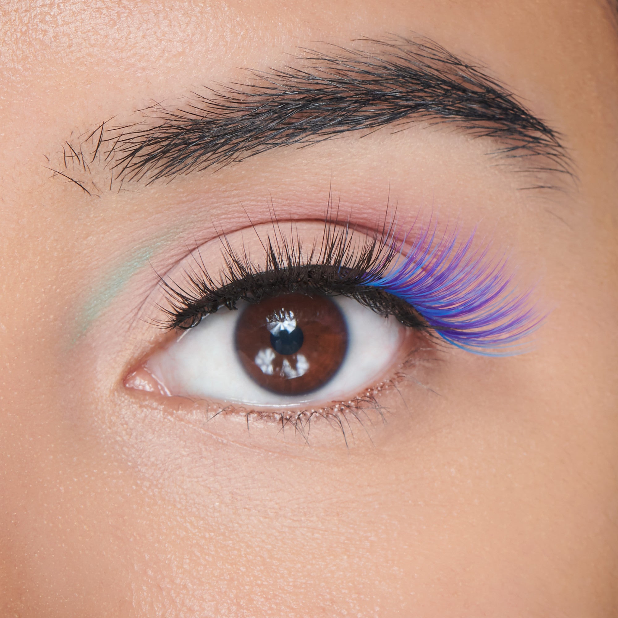 Close-up of eye with colorful makeup: pink eyeshadow, blue lower lashes, black winged eyeliner.
