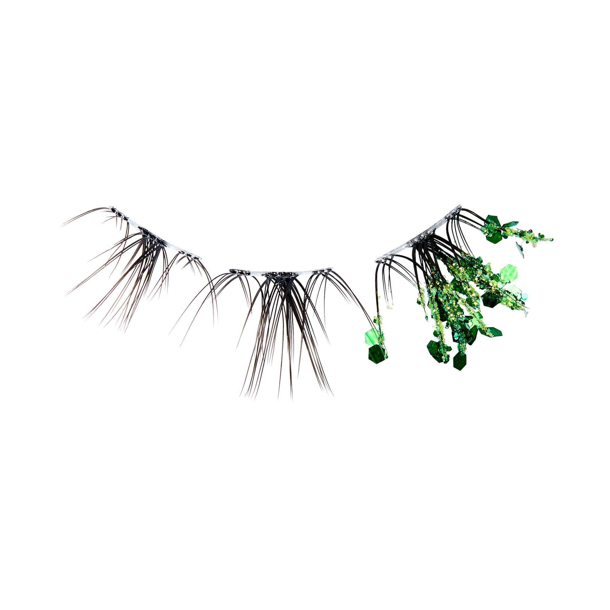 The image features a unique set of false eyelashes. The lashes are predominantly black, with a few strands extending outward, creating a dramatic effect. Interspersed among the lashes are vibrant green embellishments, resembling small crystals or decorative elements, which add a touch of sparkle and color. The overall design combines elegance with a whimsical, nature-inspired aesthetic.