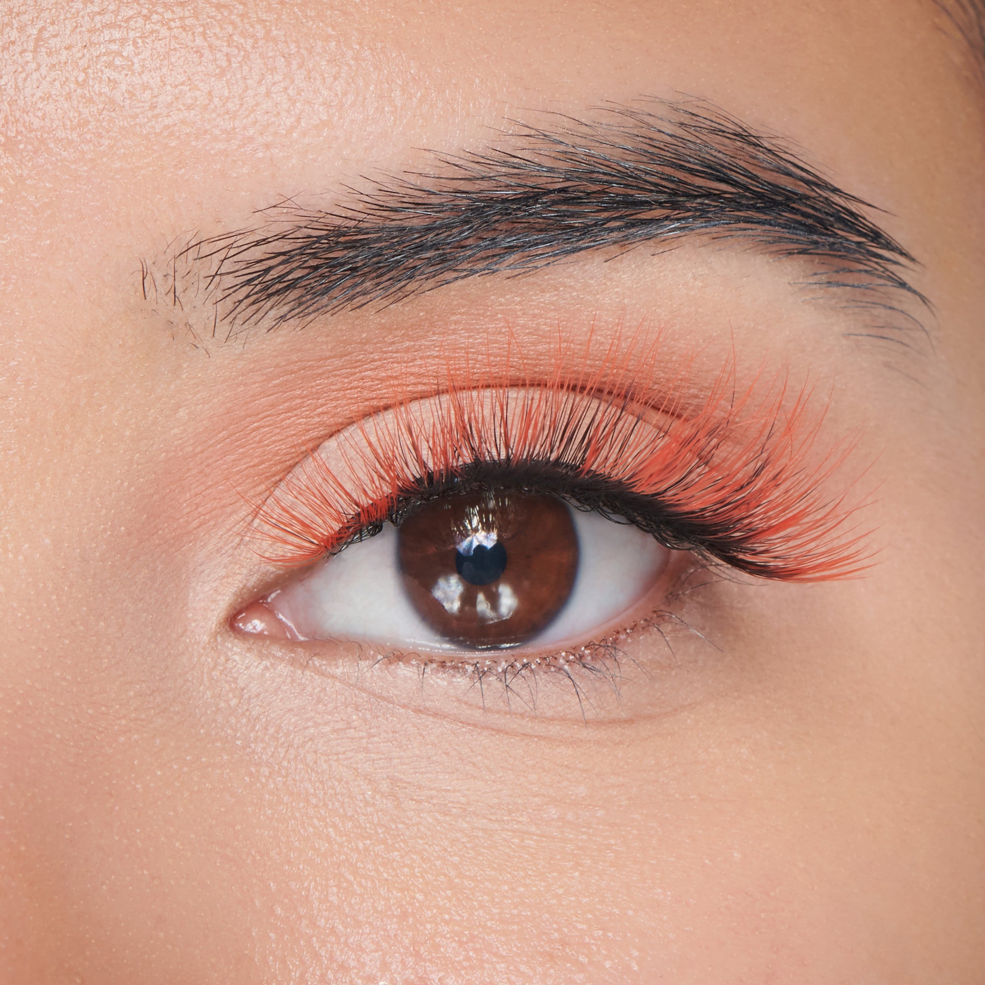 Close-up of a brown eye wearing black false eyelashes with bright orange tips, complementing Halloween-themed makeup.