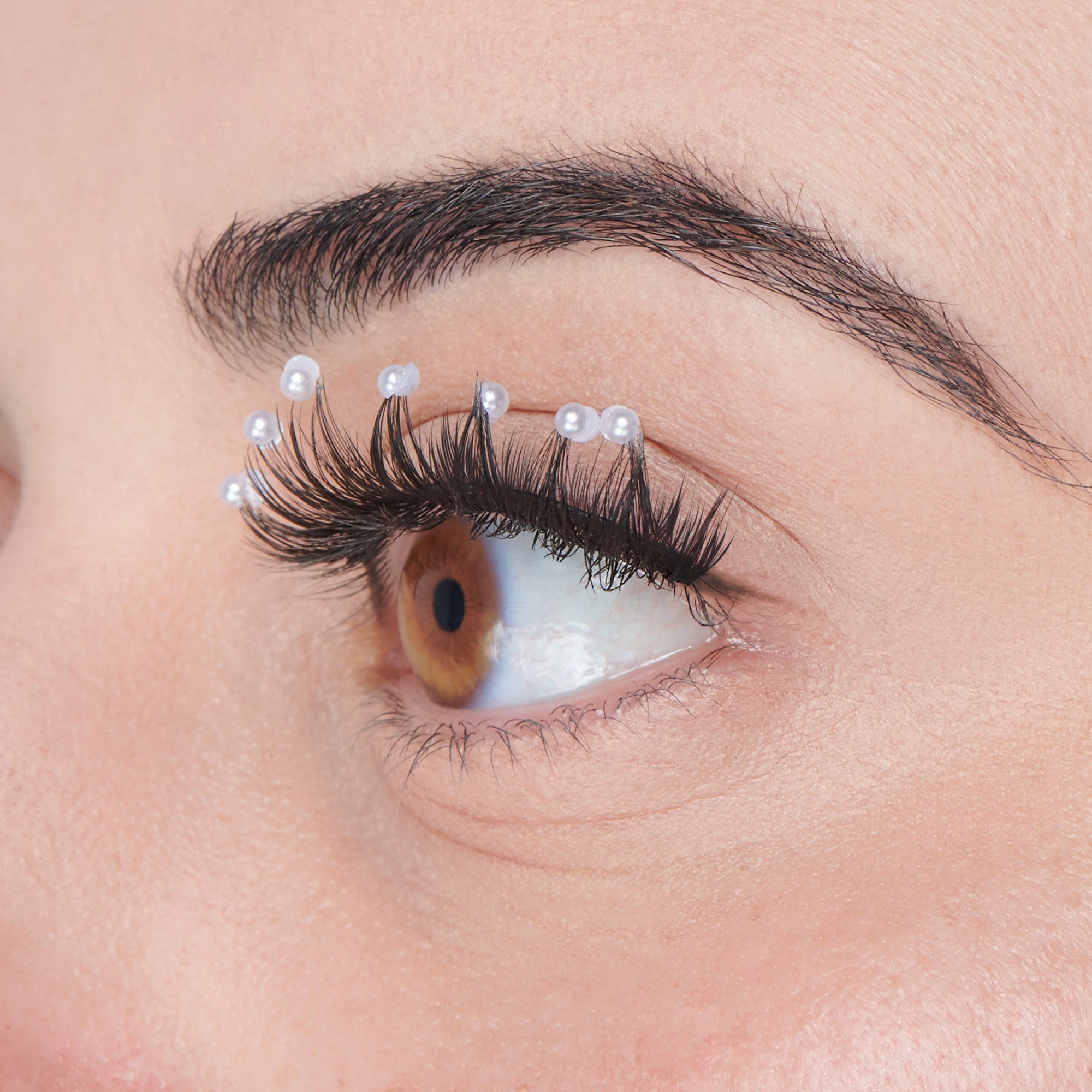 Close-up side view of an eye with decorated black false eyelashes featuring small white pearl-like gems attached along the lash line.