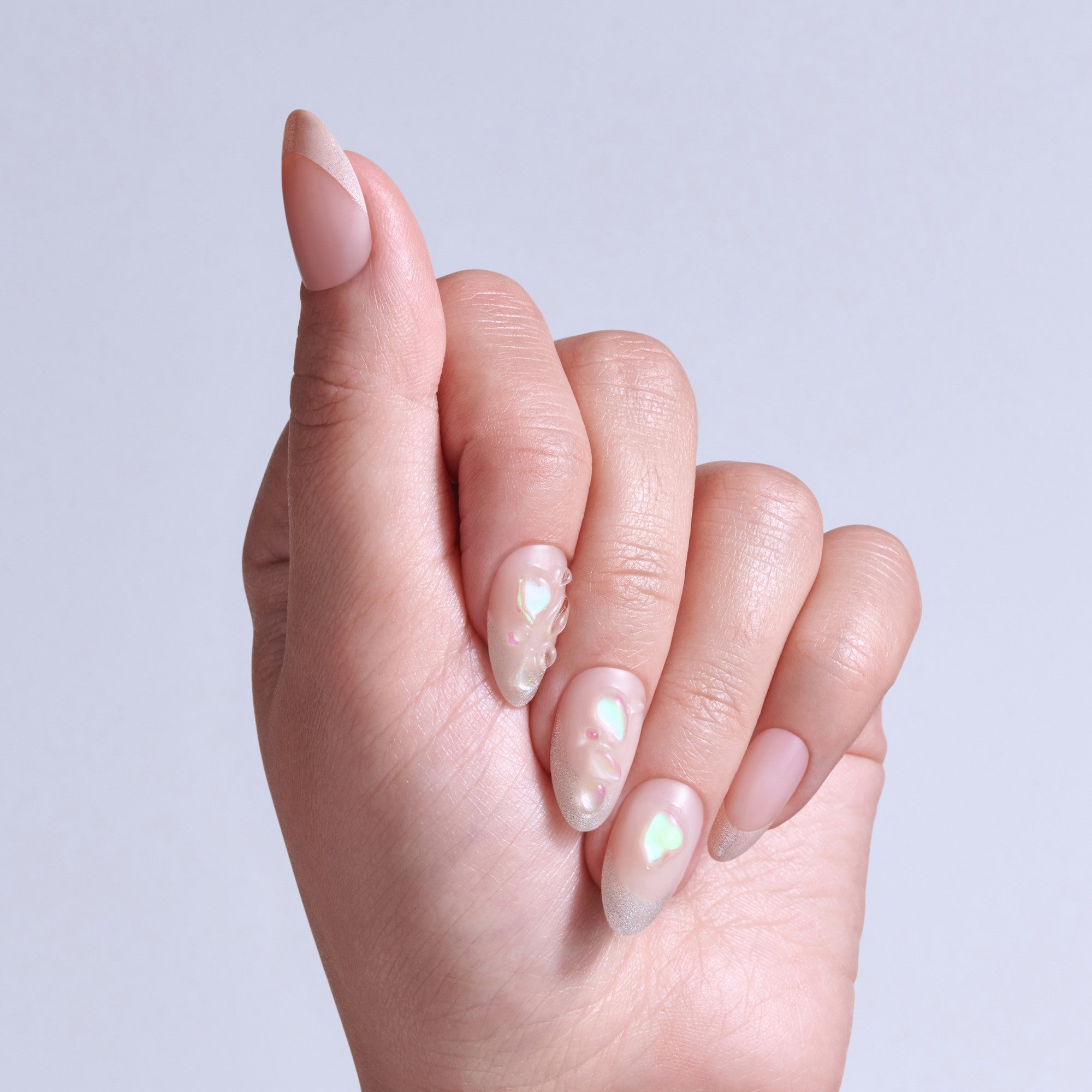 Hand displaying almond-shaped nails with iridescent pearl nail polish and rhinestone accents.