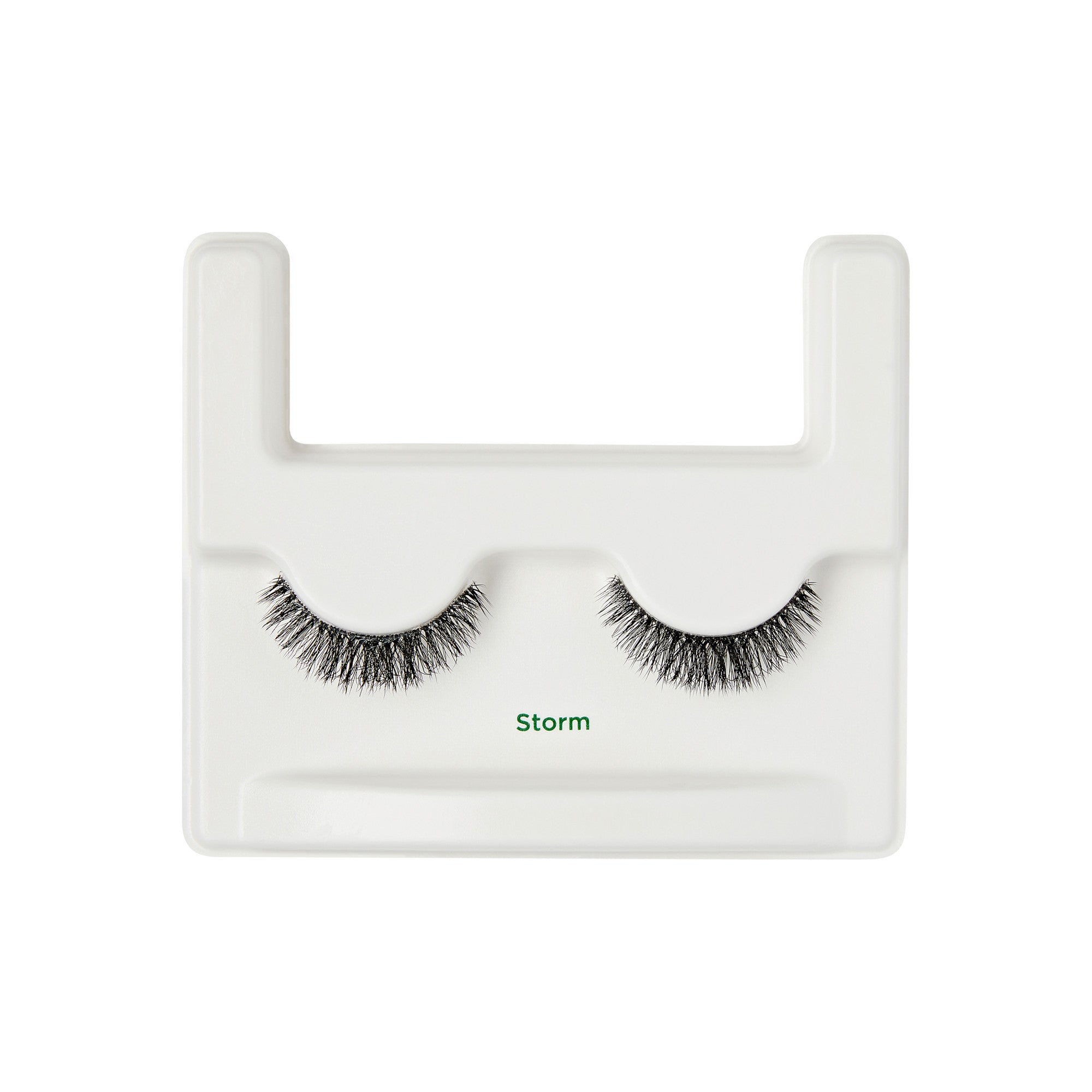 The image shows a pair of false eyelashes displayed on a white plastic holder. The eyelashes are labeled "Storm" in green text. The holder has a U-shaped design with two protruding sections at the top, which help to keep the eyelashes in place. The eyelashes are dense and have a slightly curved shape, designed to enhance the appearance of the eyes when worn.
