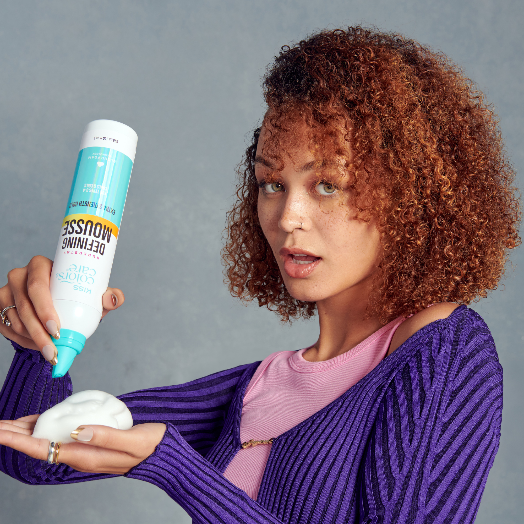 Woman holding a bottle of hair product against a gray background