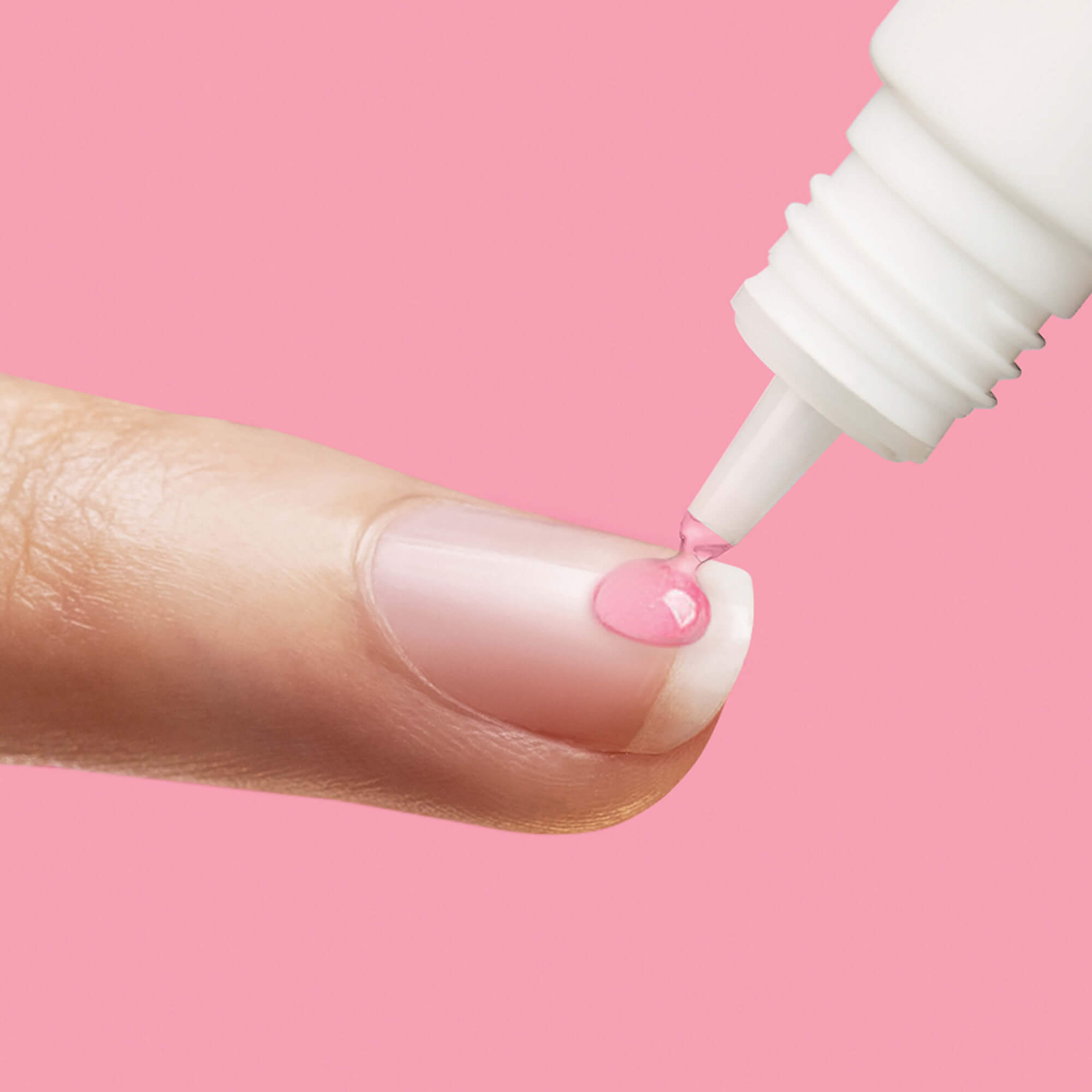 Pink nail polish being applied to fingernail with brush applicator against pink background.