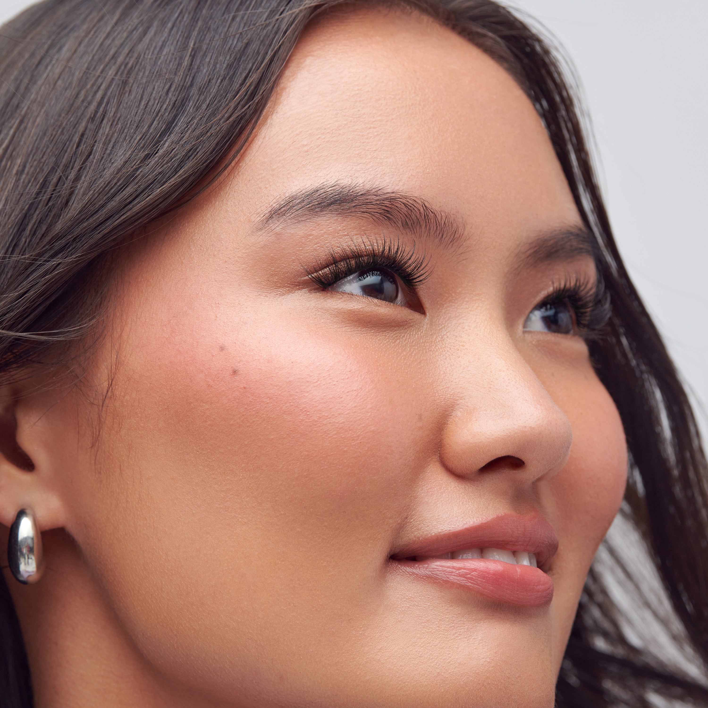 Close-up portrait of woman with dark hair, bold eyelashes, and hoop earrings.