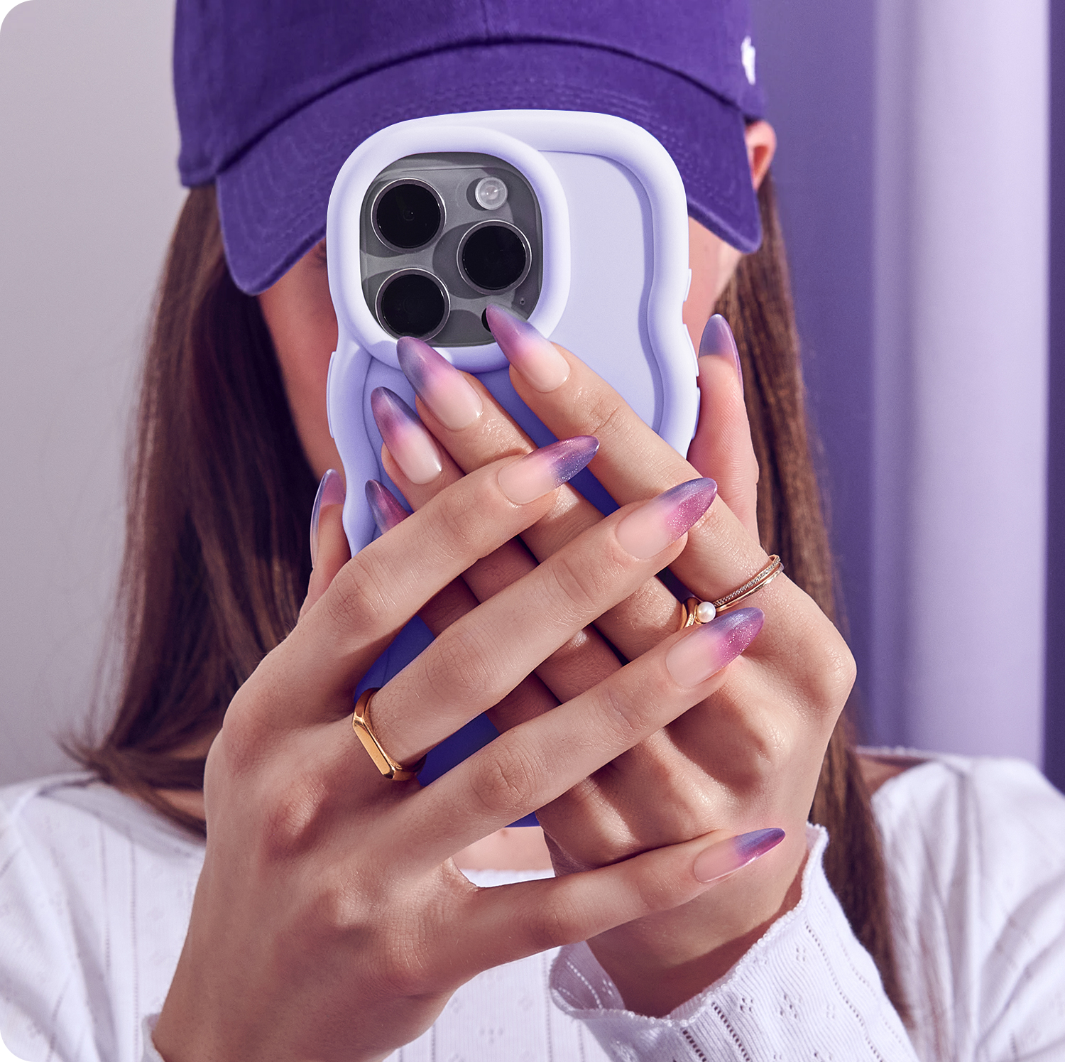 Person holding a phone with a purple case, wearing a purple cap and white shirt.