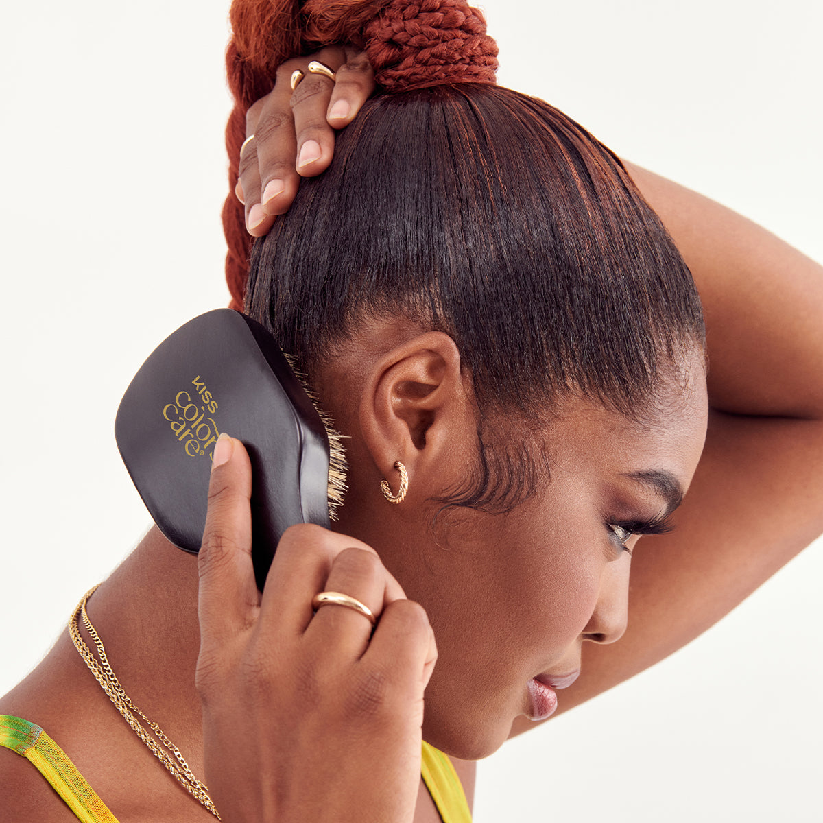 Woman with braided hair using a black Kiss Color and Care hairbrush, close-up side profile showing smooth, styled edges and gold jewelry.