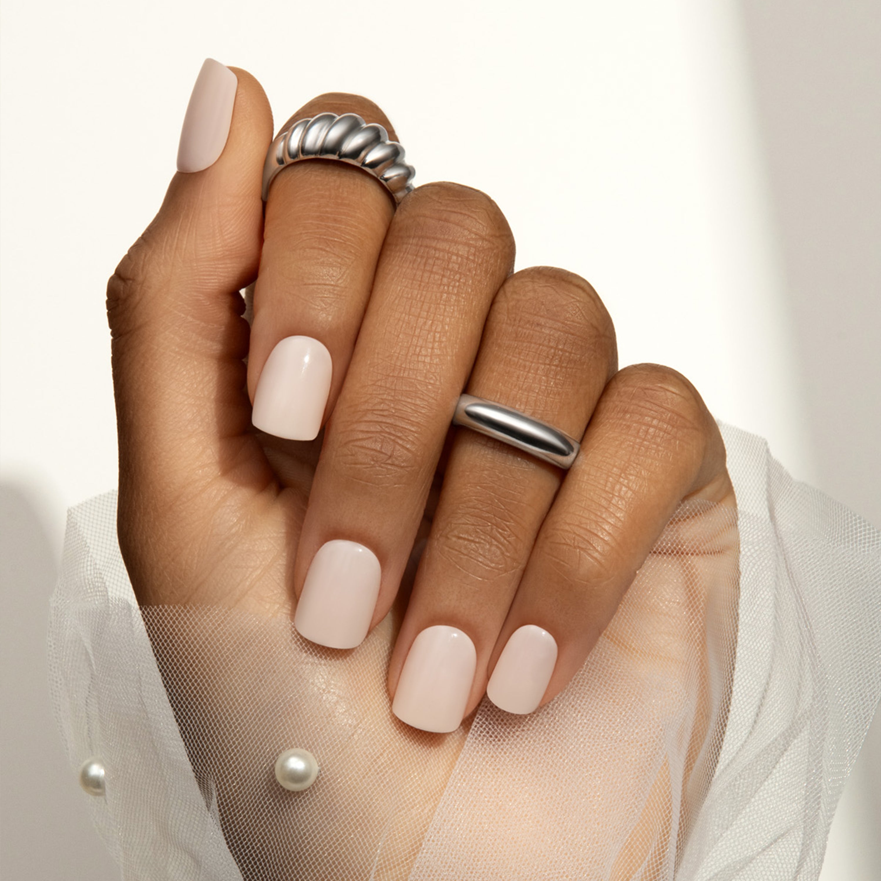 Hand with light pink press on nails and silver rings on a neutral background