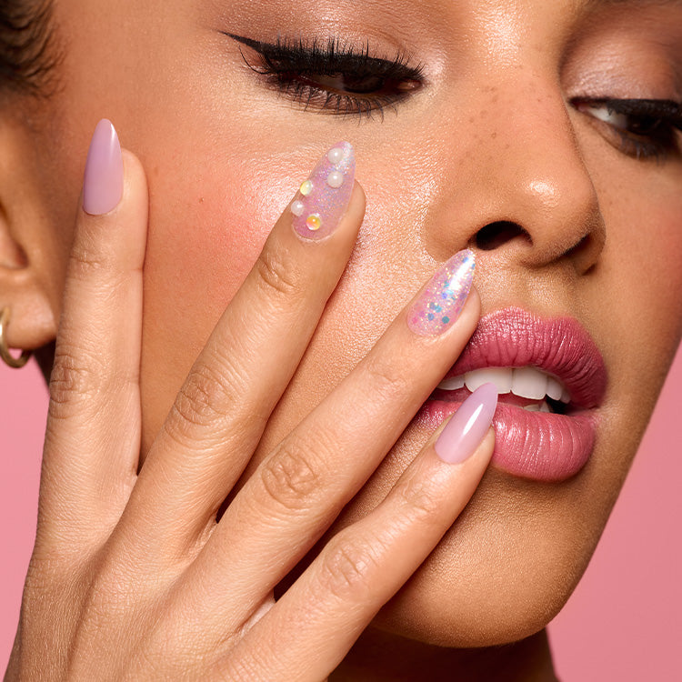 A woman with her hand against her face, showcasing an almond shaped manicure in varying light pink glittery designs