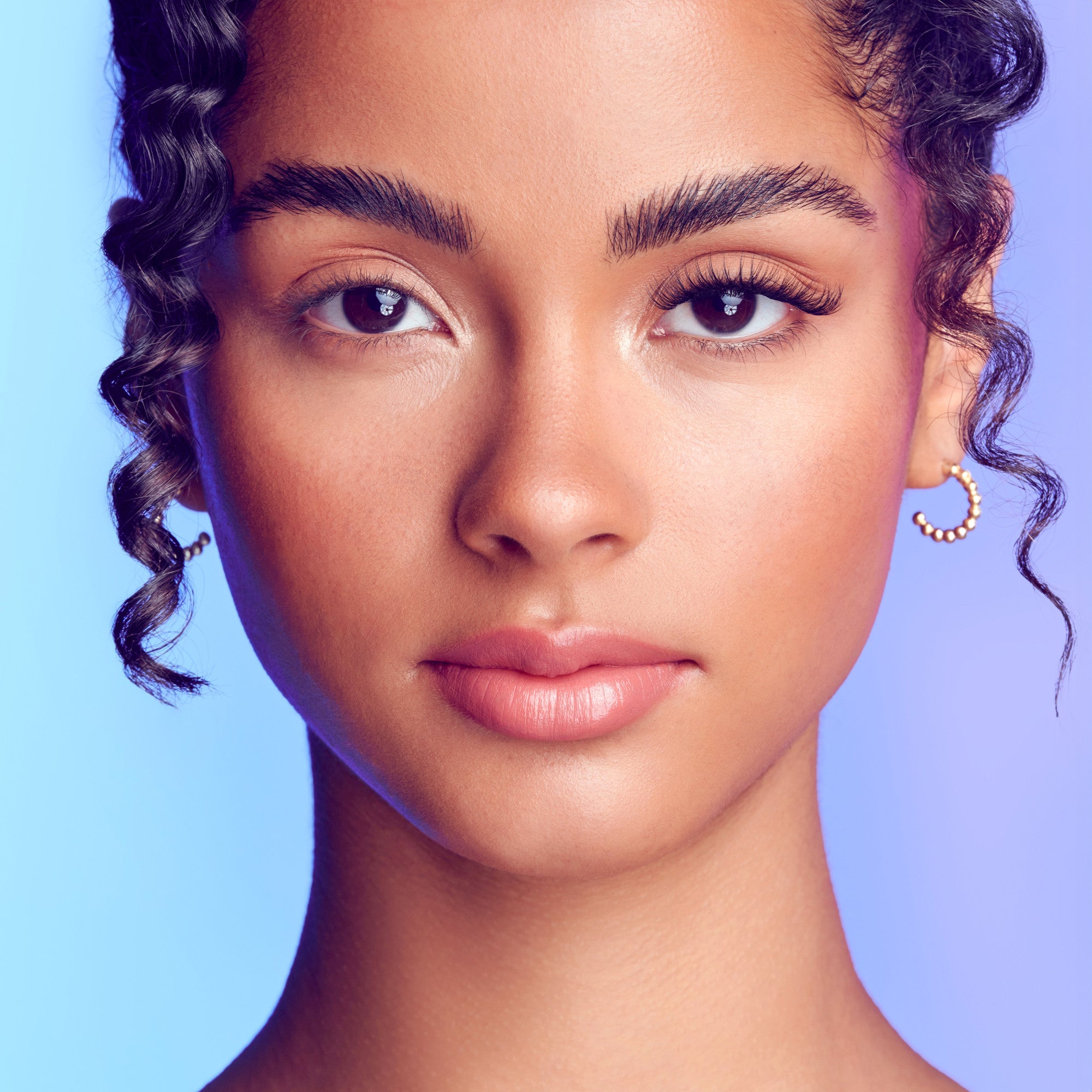 The image features a close-up portrait of a young person with curly hair. They have a smooth complexion and well-defined features, including prominent eyebrows and full lips. The background is a gradient of blue hues, which enhances the subject&