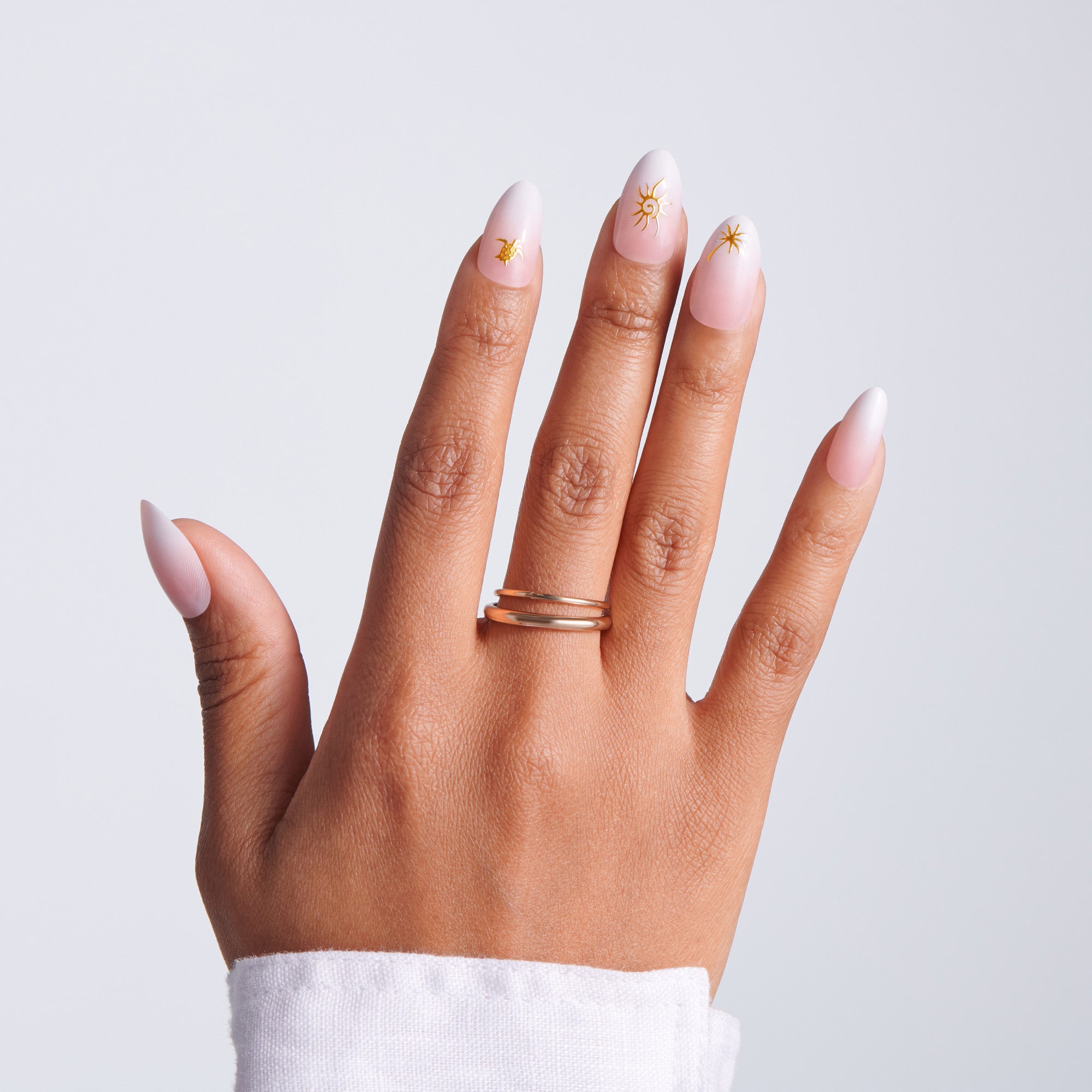 Hand with pink nail polish and a gold ring on a light gray background