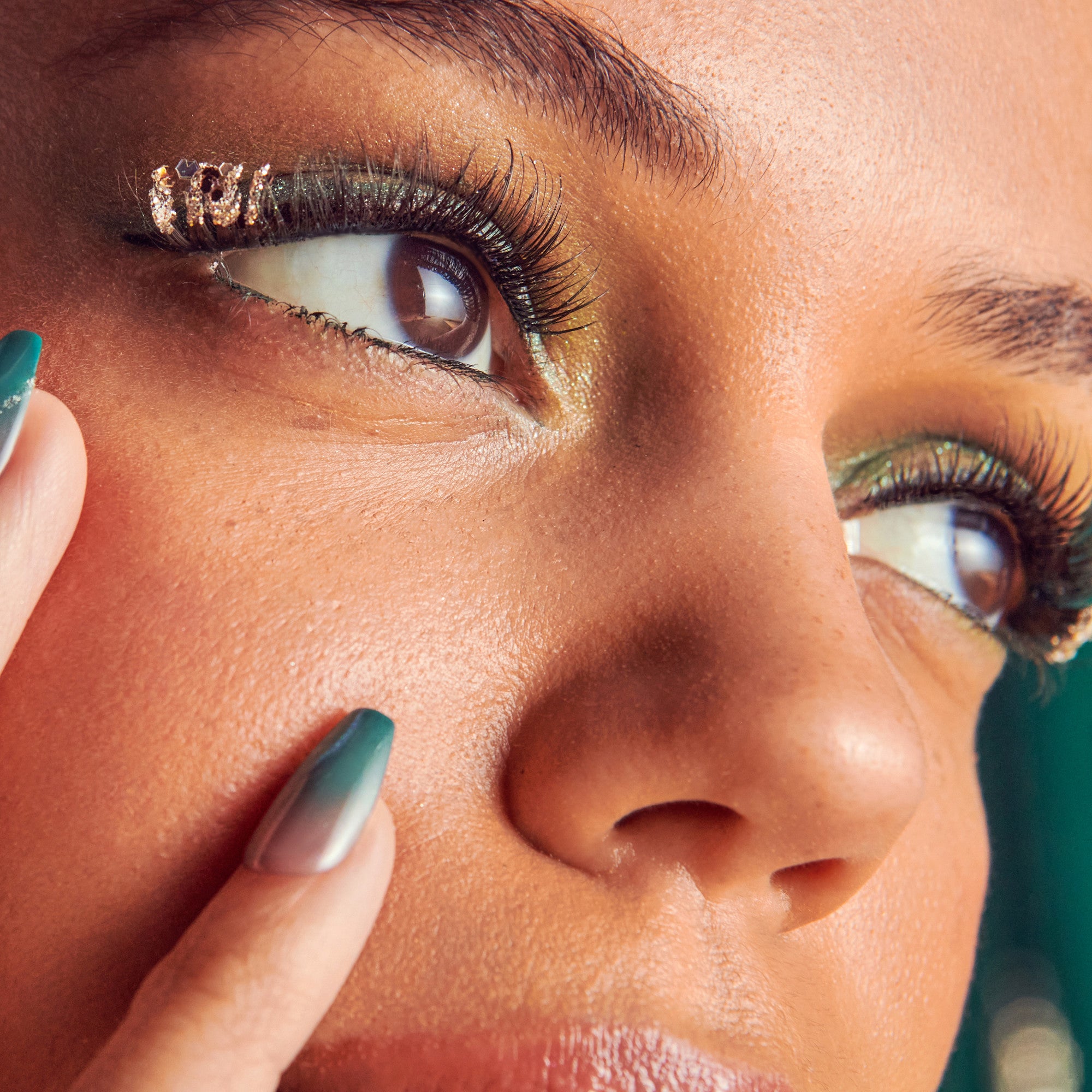 Close-up of eye makeup with gold eyeshadow, black eyeliner, and teal ombre nails