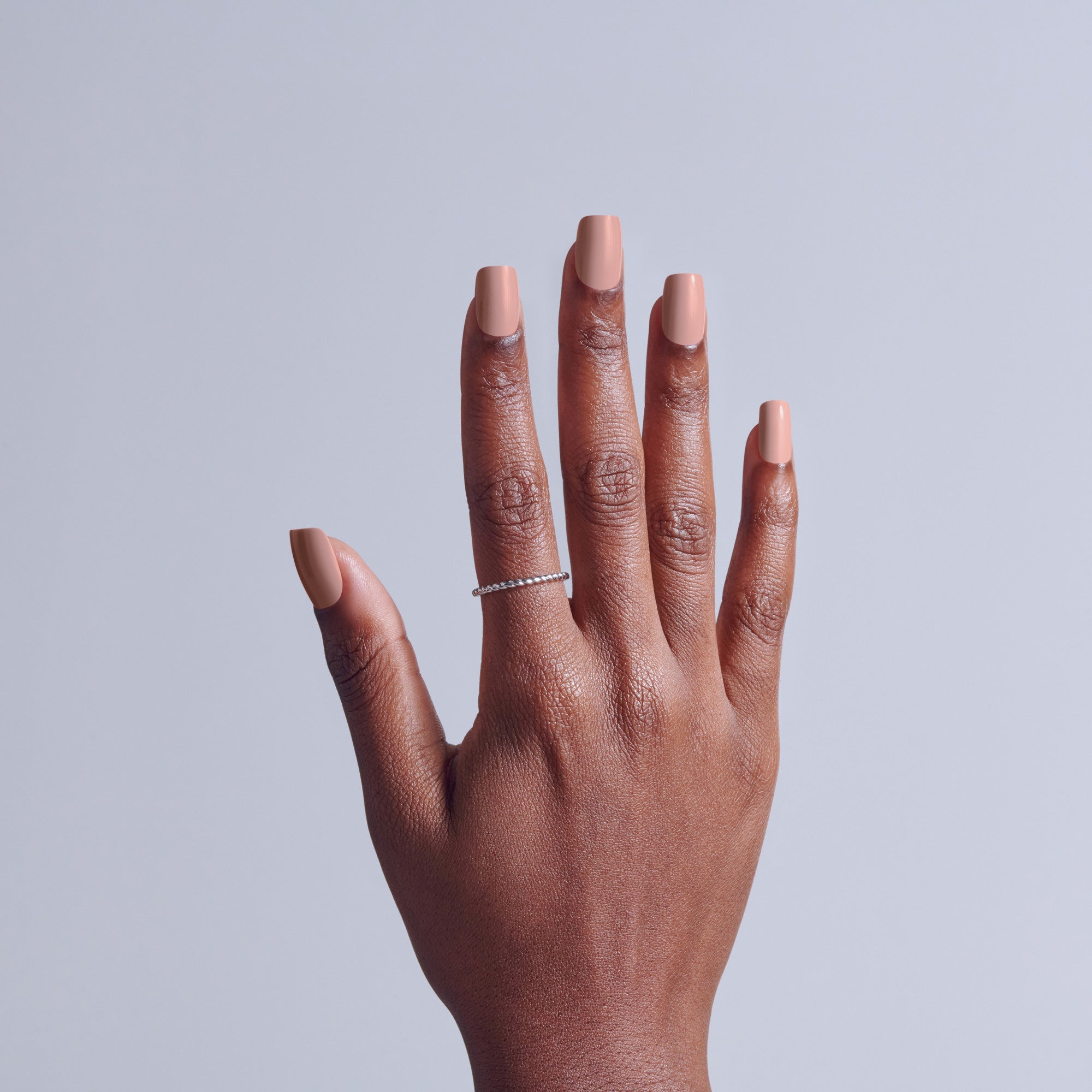 Hand with neutral nail polish and diamond ring on light background.