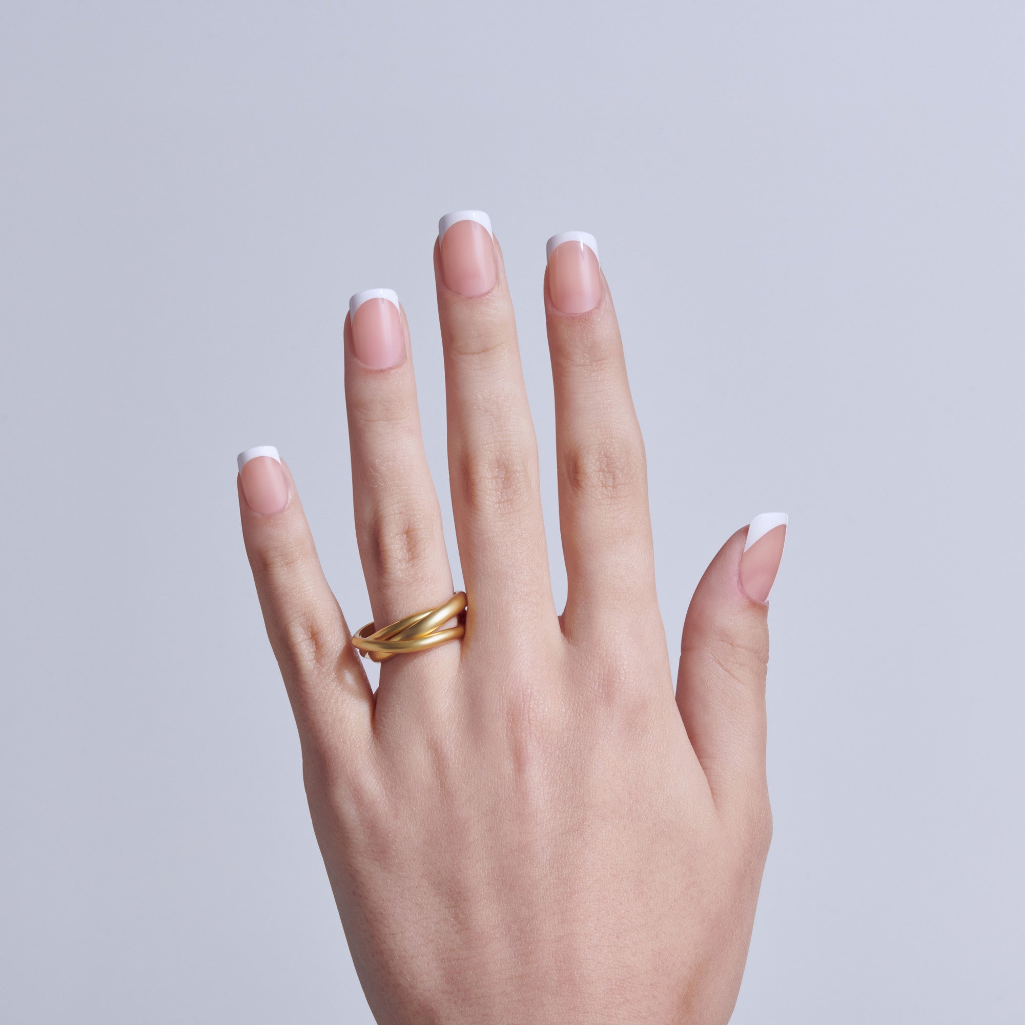 Hand displaying classic white French manicure with gold band ring on light background.
