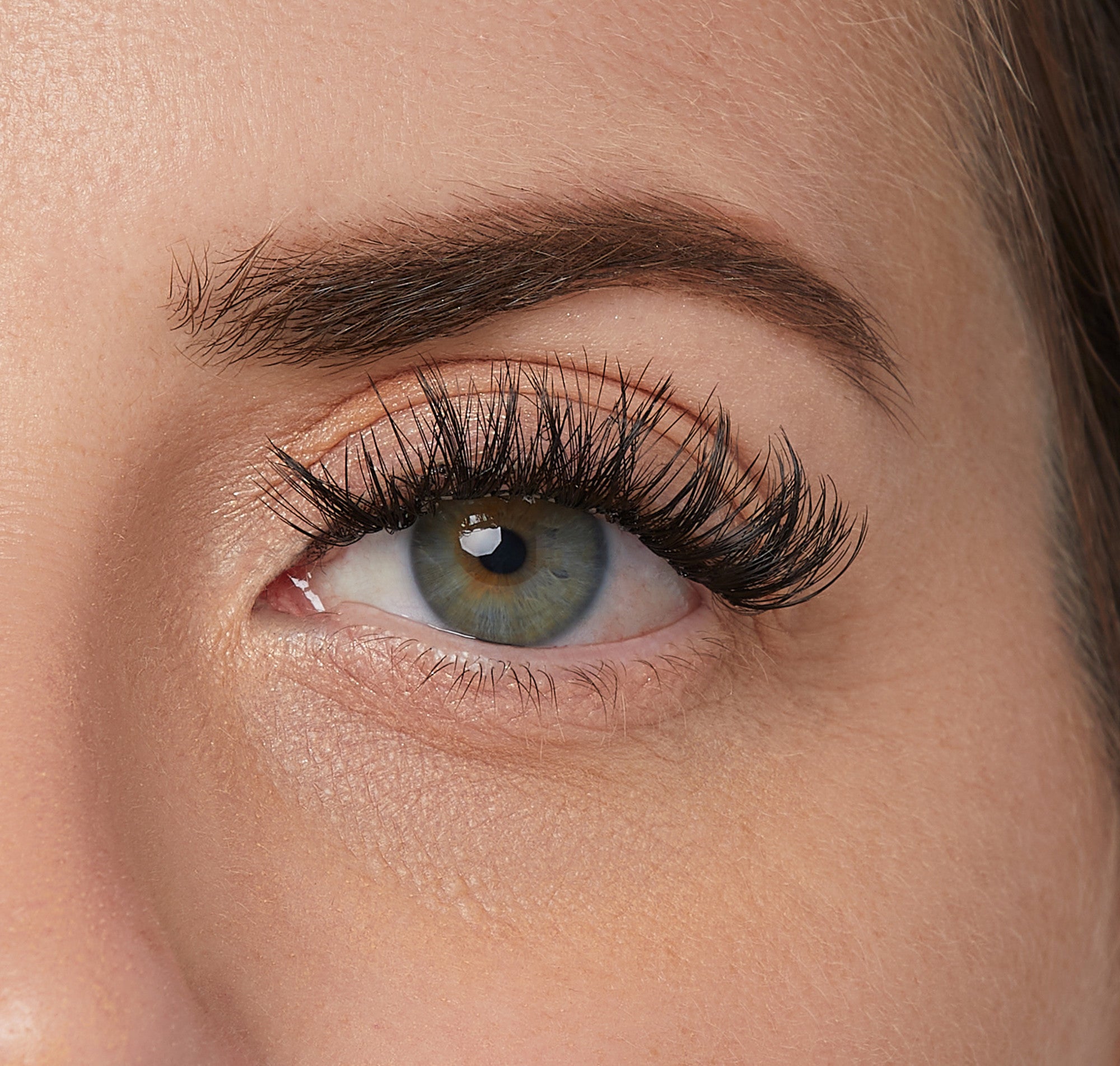 Close-up of a green eye with long, full, and curled black false eyelashes applied, showing the dramatic \