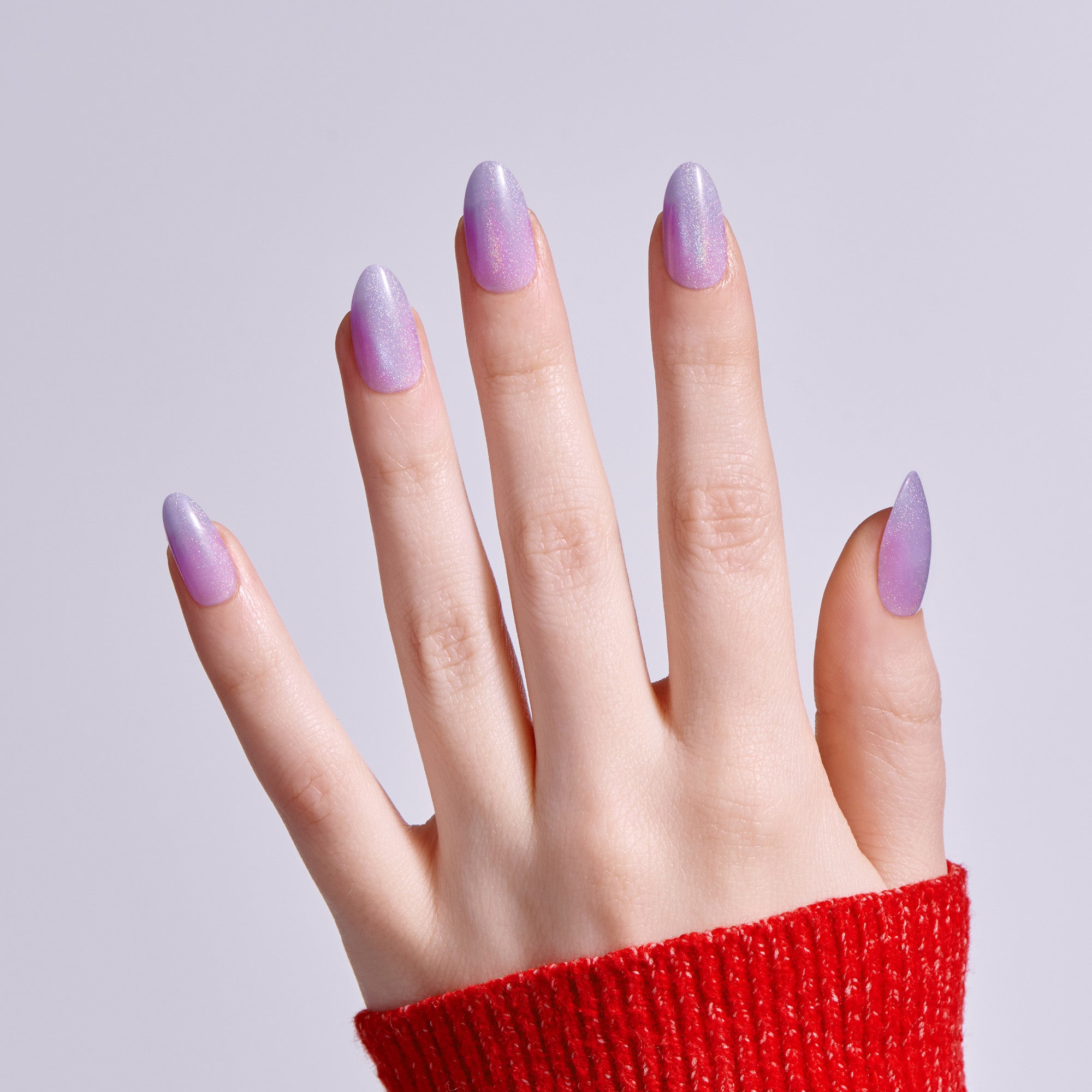 Hand with purple shimmer nail polish manicure against light background.