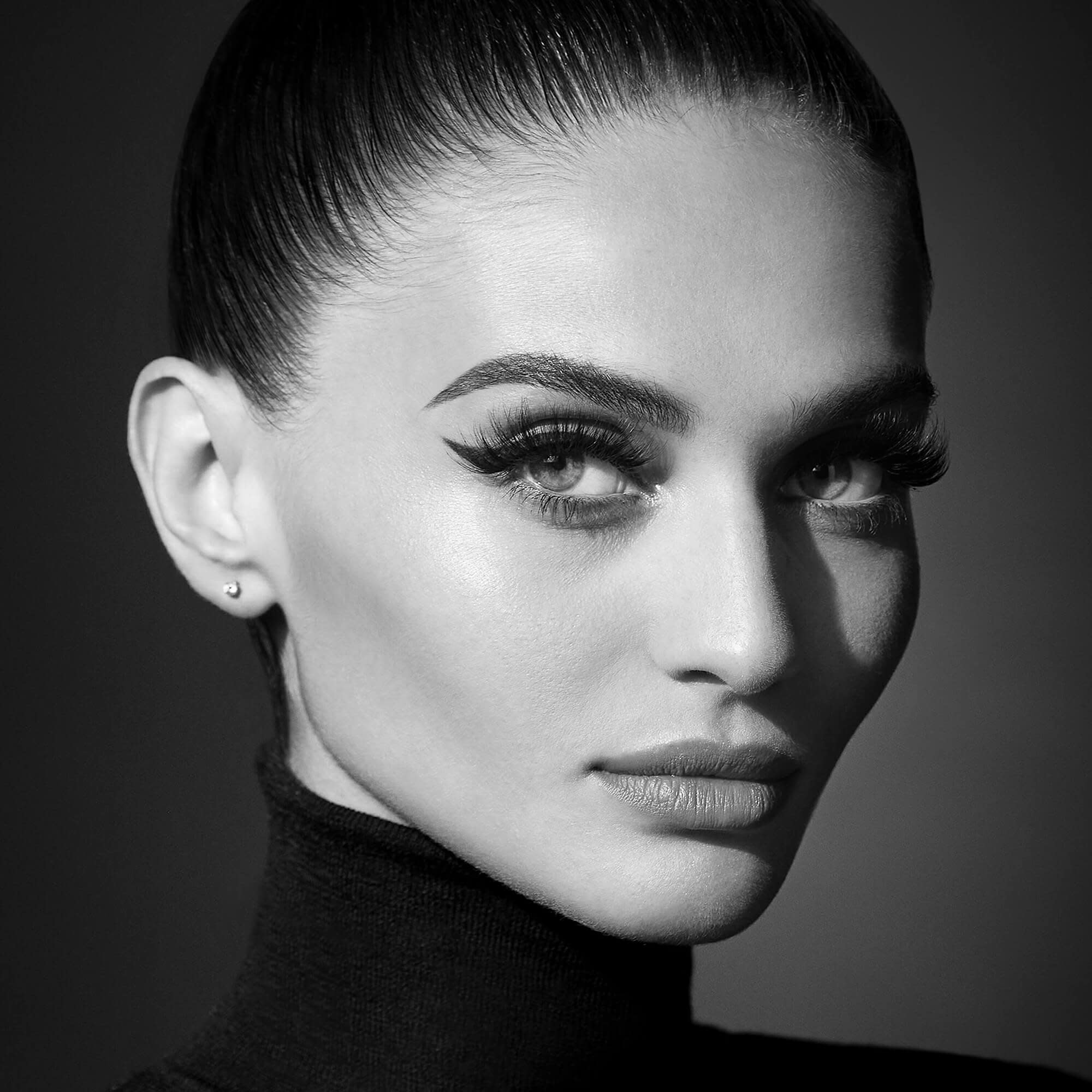 Black and white portrait of woman with sleek pulled-back hair and dramatic winged eyeliner.