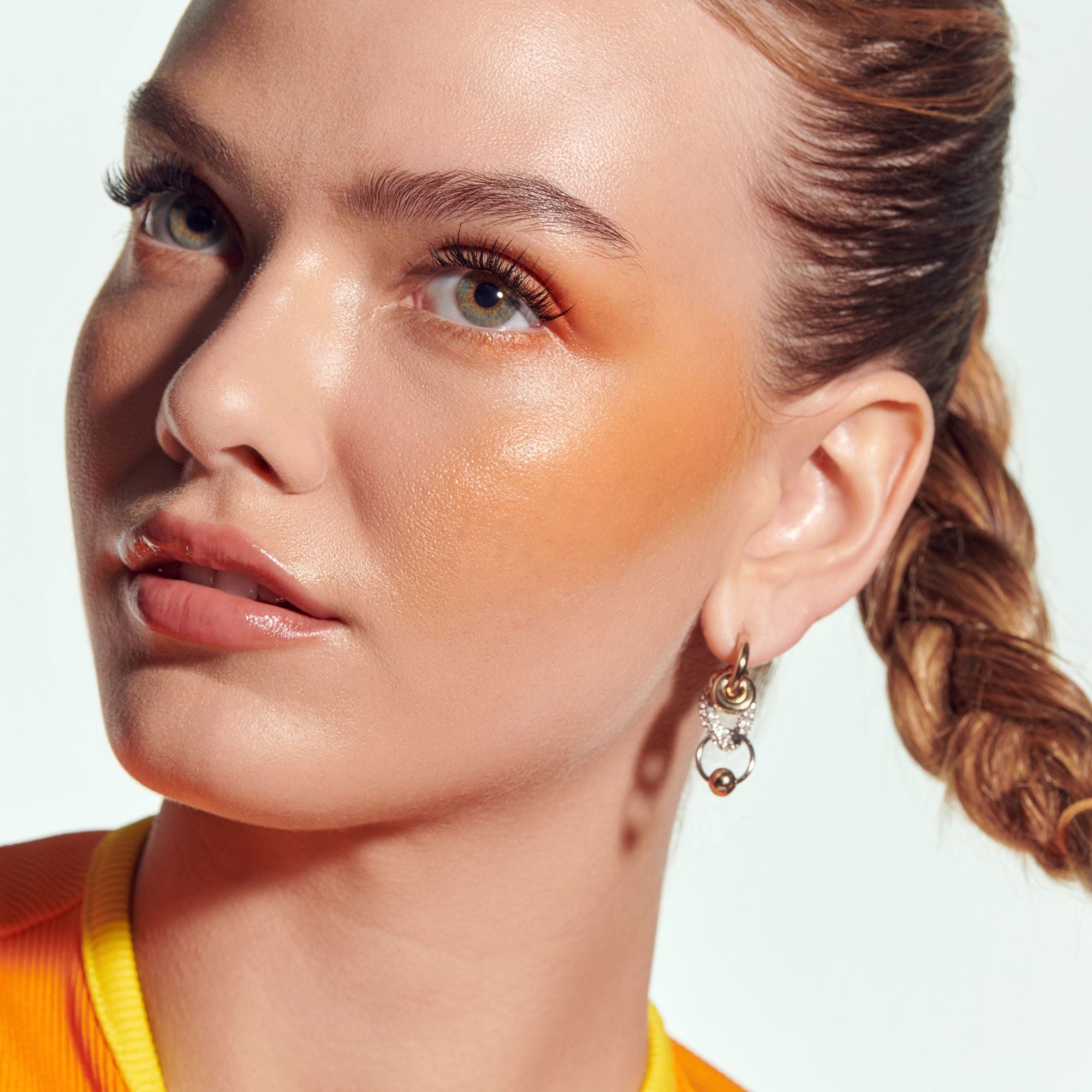Close-up of a woman with a sun-kissed glow, wearing earrings against a neutral background