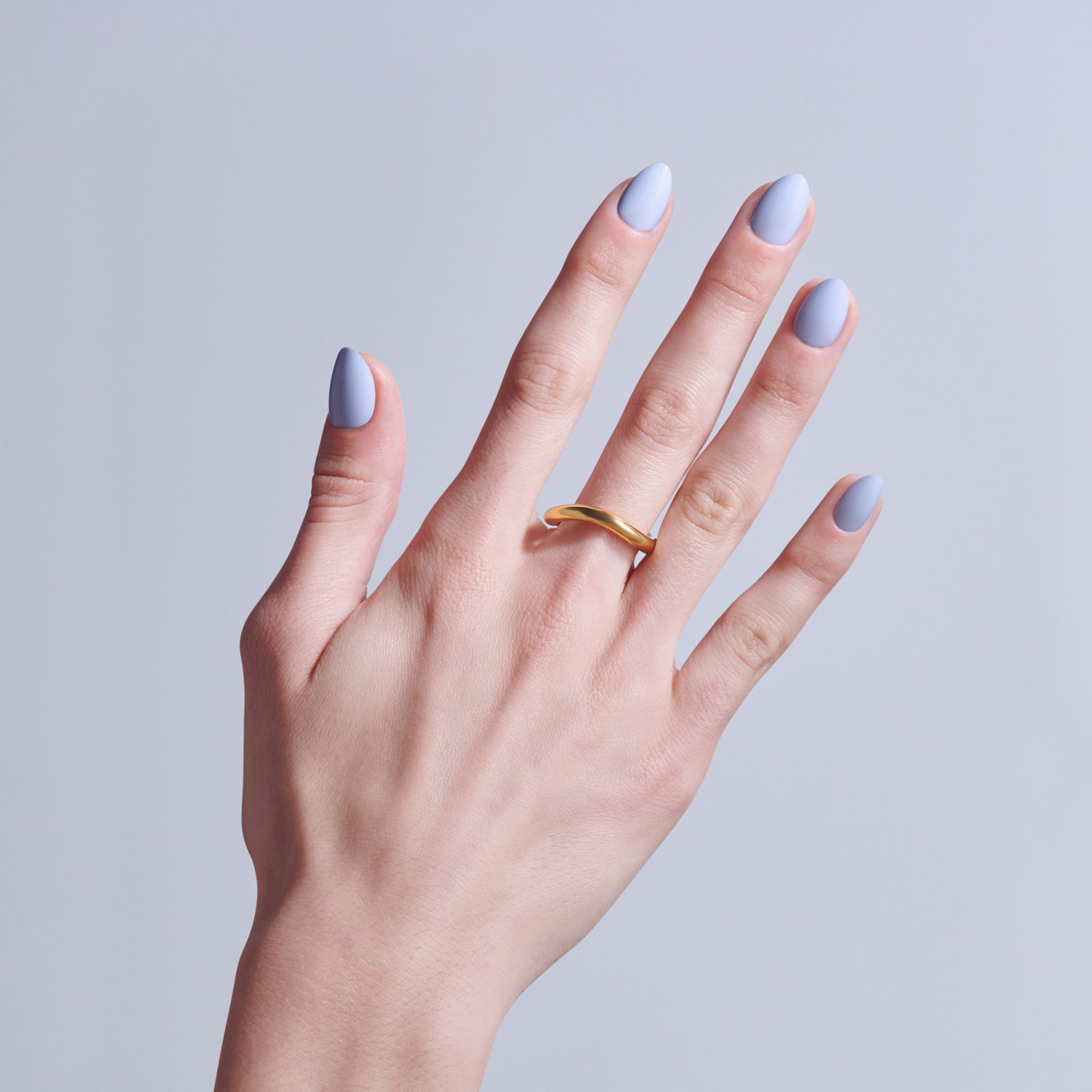 Hand with lavender and white ombre nails wearing gold band ring