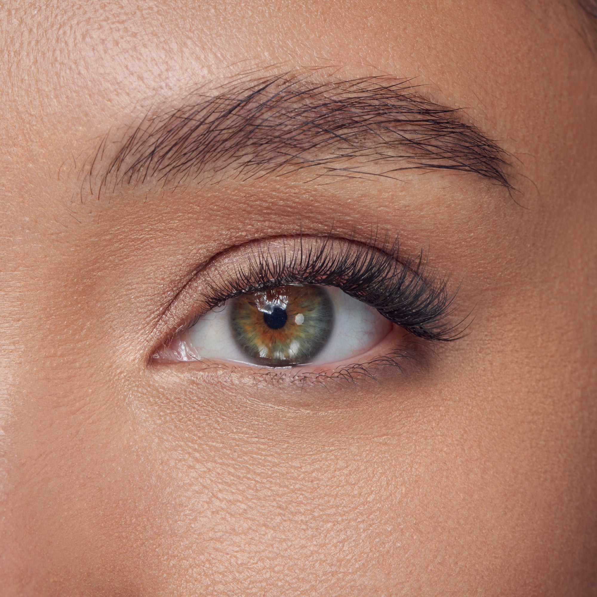 Close-up of a greenish eye with individual black lash extensions applied, showing natural-looking volume and length on the upper lashes.