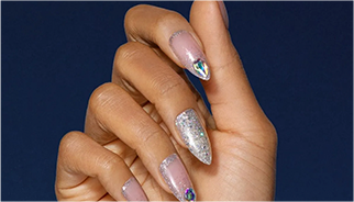 A hand with long, decorated, stiletto-shaped nails, one with silver glitter design and the other nails with silver metallic