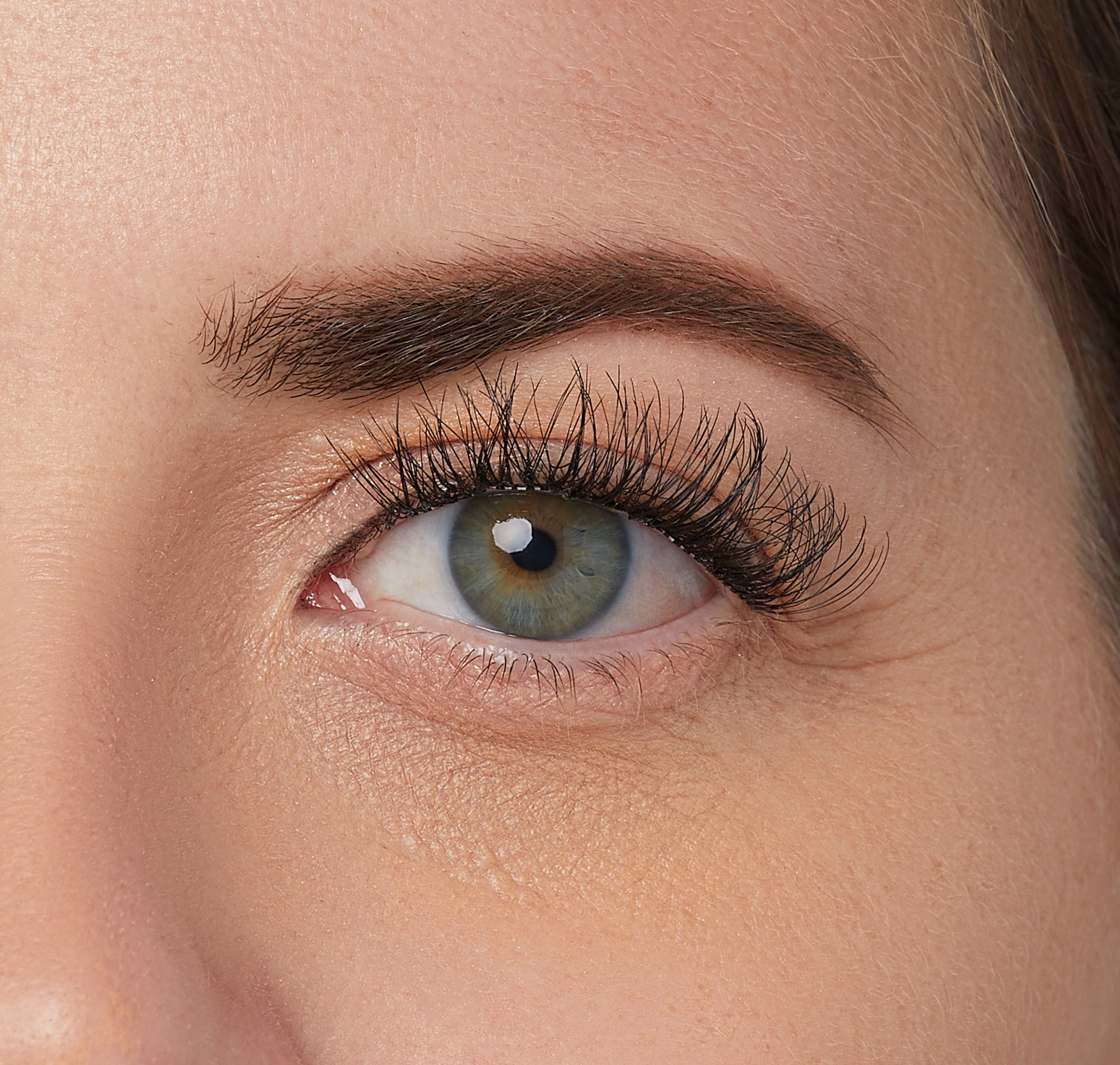 Close-up view of a green eye with natural-looking, voluminous false eyelashes applied to the upper lash line.