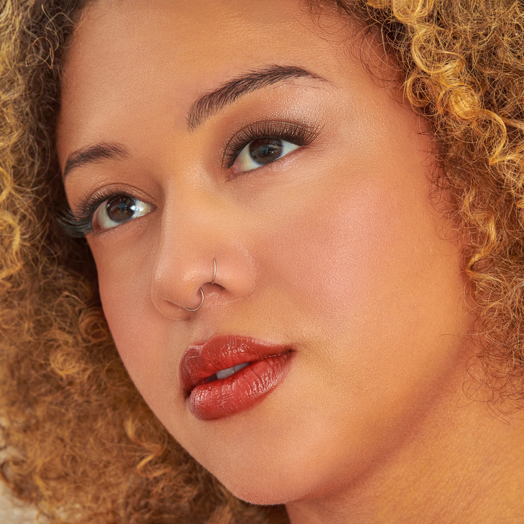 Woman with curly golden hair, nose ring, and red lipstick in profile view.