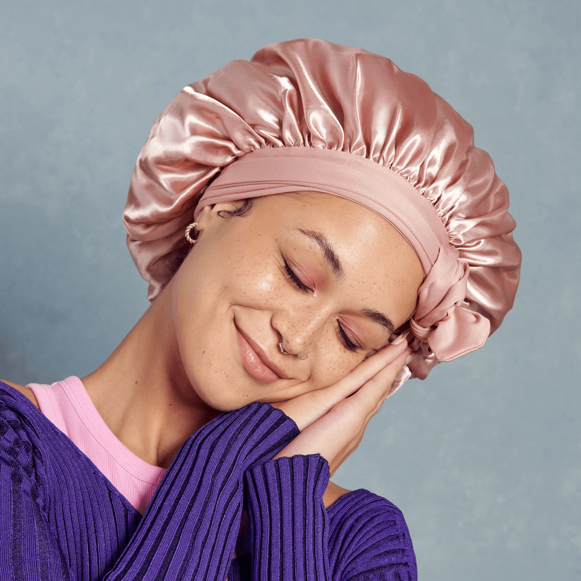 Woman wearing a pink satin bonnet against a gray background