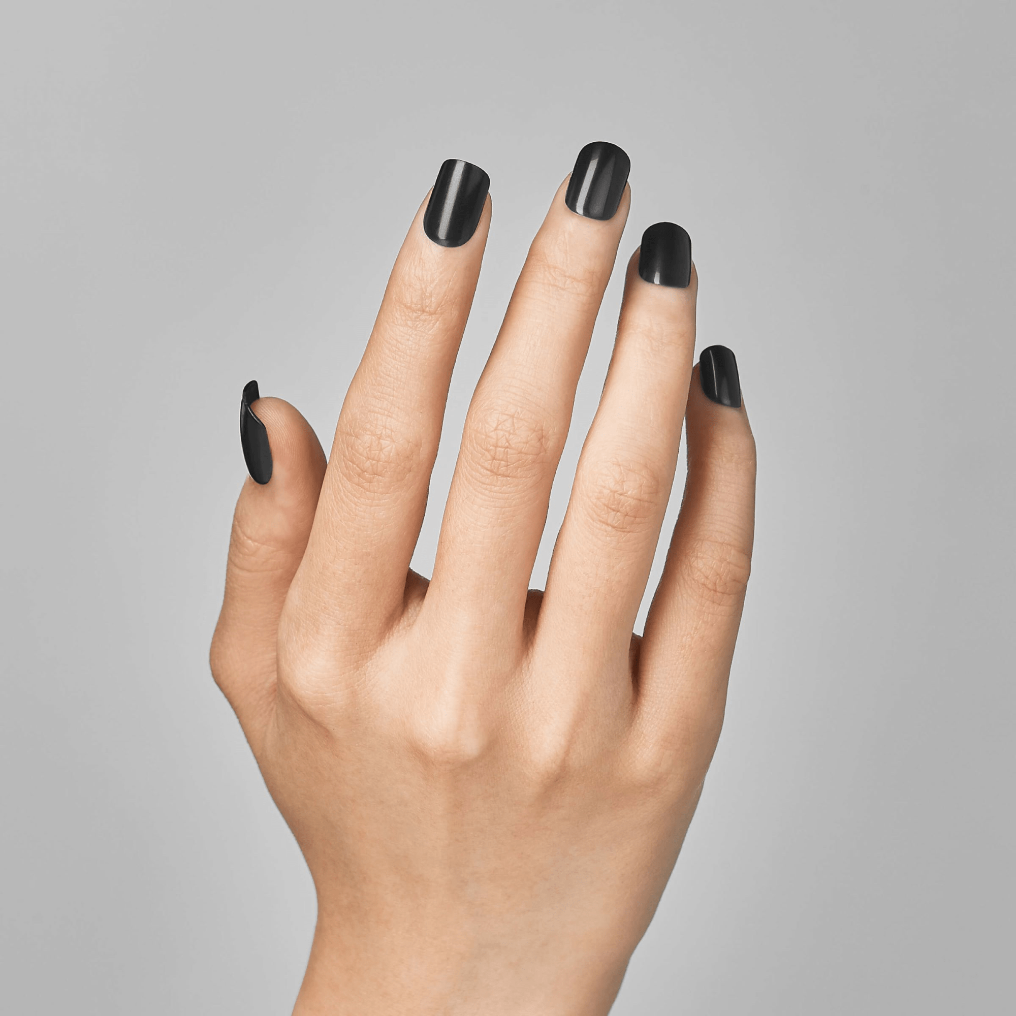 Hand with nails painted in solid glossy black, shown against a plain light gray background, displaying medium-length, square-shaped press-on nails.