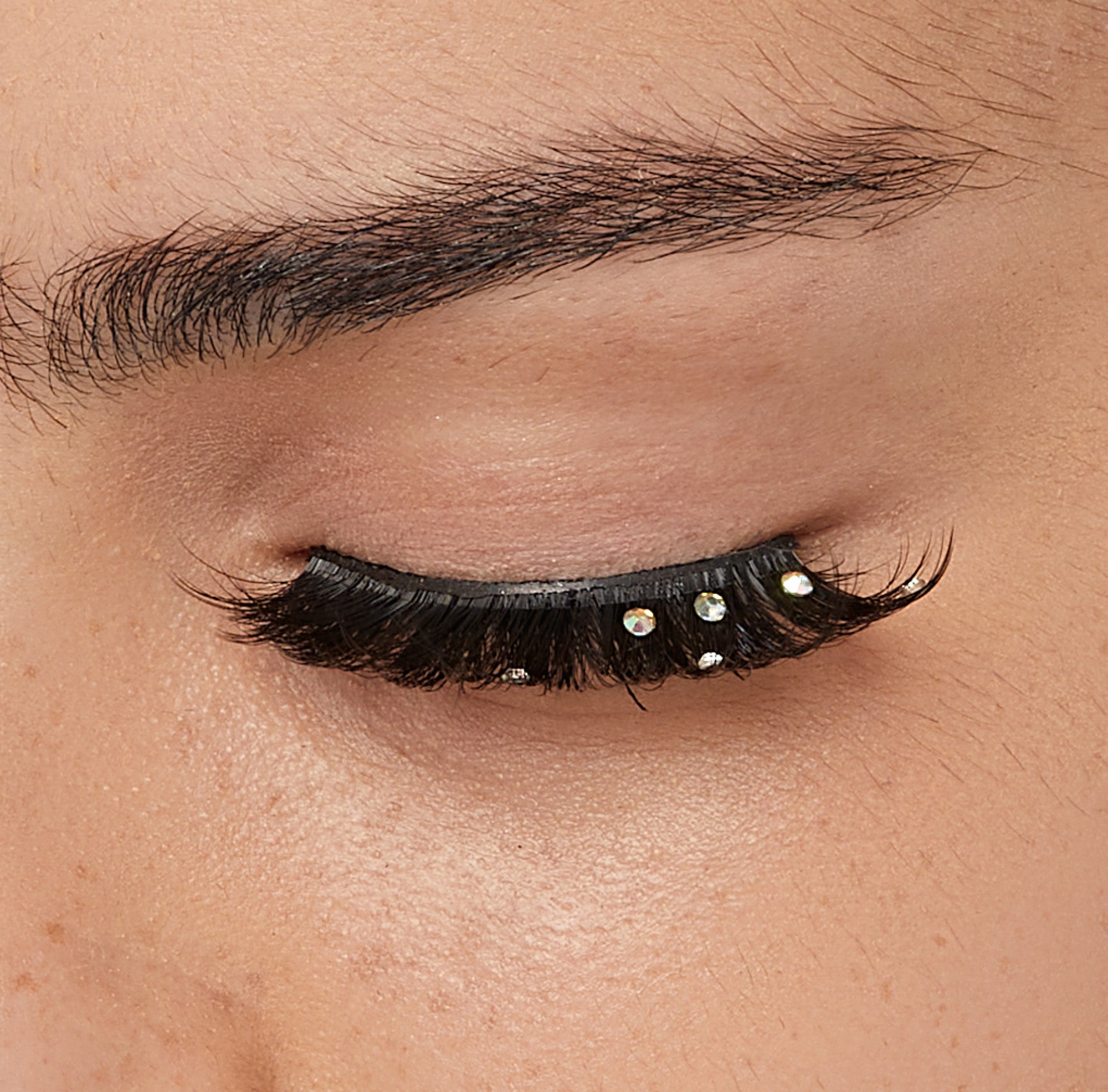 Closed eye with black volumized false lashes and iridescent rhinestone embellishments.