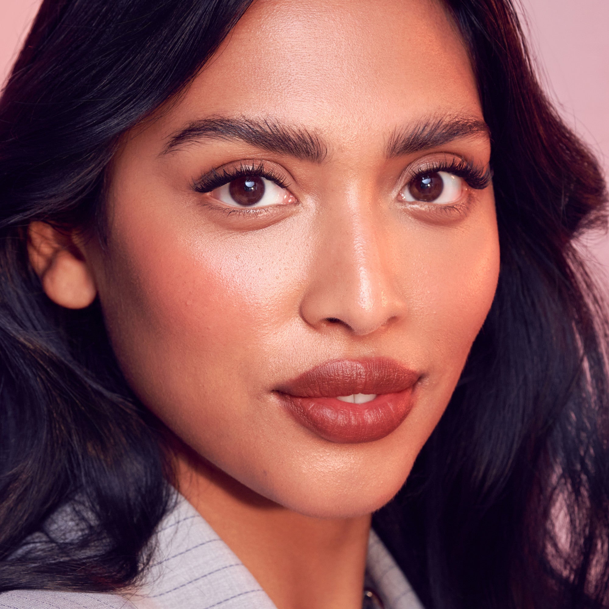 Close-up of a woman with dark hair and makeup on a pink background