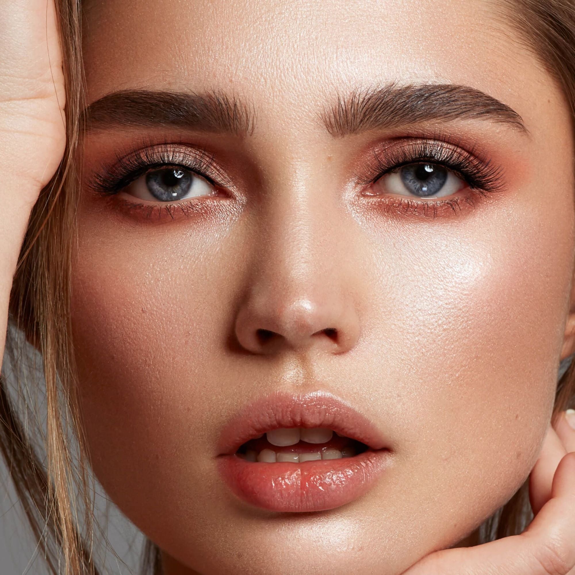 Close-up portrait of woman with blue eyes, defined eyebrows, and nude makeup look.