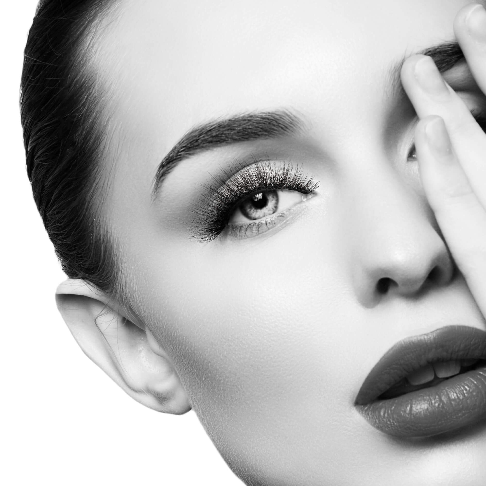 Black and white portrait of woman with defined eyebrows and lashes, touching her face.