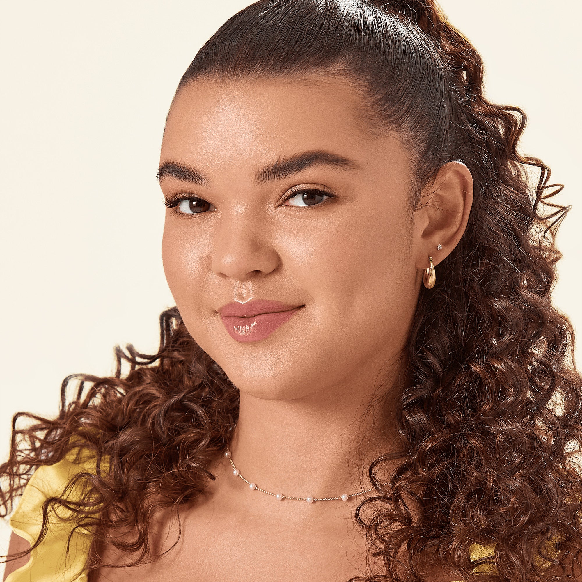 Close-up of a woman with smooth, self-adhesive false eyelashes applied, wearing a yellow top and pearl necklace, showcasing natural, sleek eye makeup.