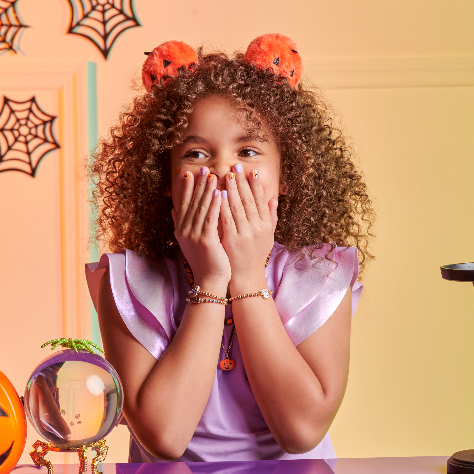 Child wearing Halloween-themed headband with pumpkin design, sitting at a table with decorative items.