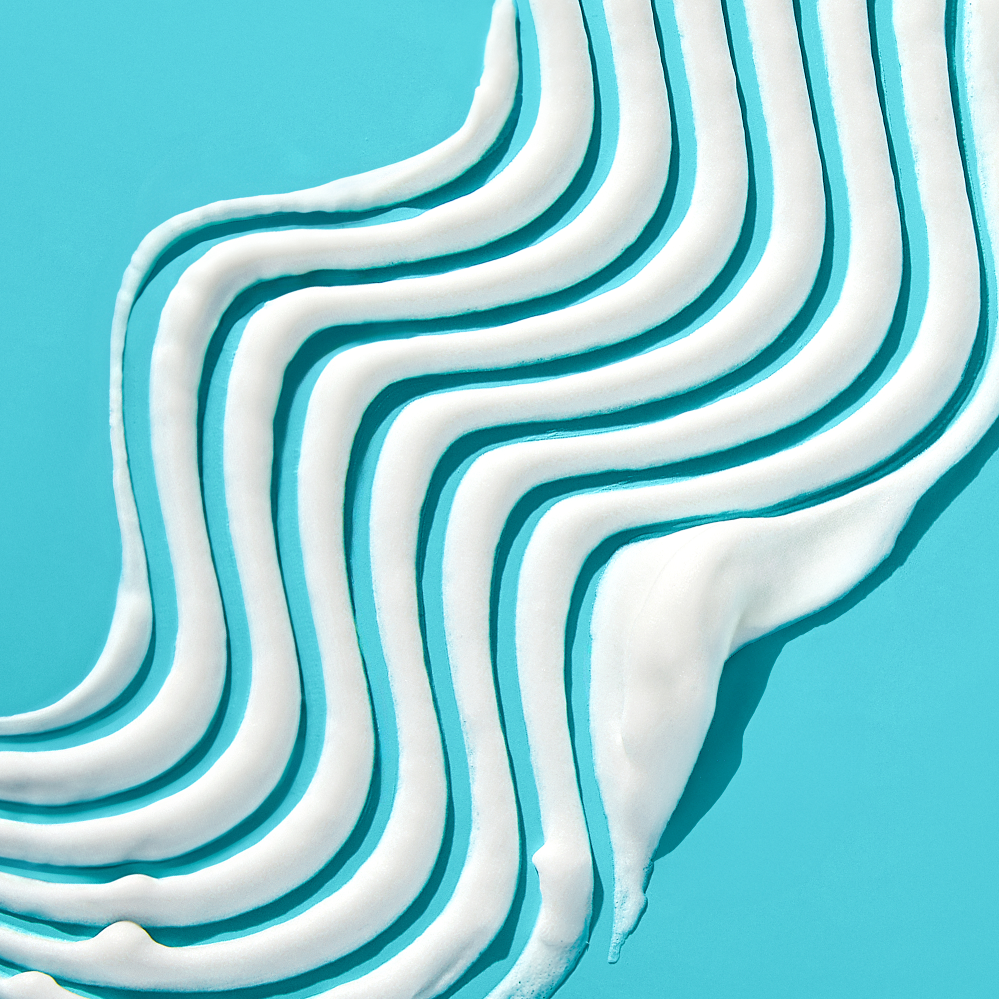 White styling mousse foam spread in curved stripes on a bright turquoise background, emphasizing smooth texture and volumizing effect.