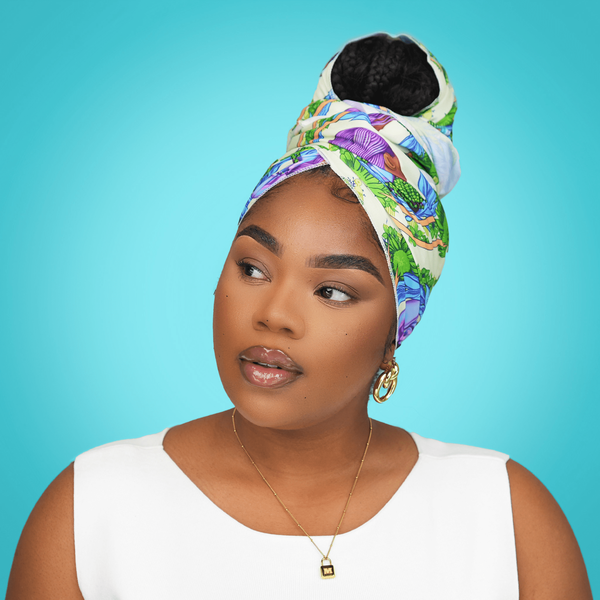 Woman wearing a limited edition satin wrap scarf with green, blue, and purple patterns, styled in a high bun against a turquoise background.