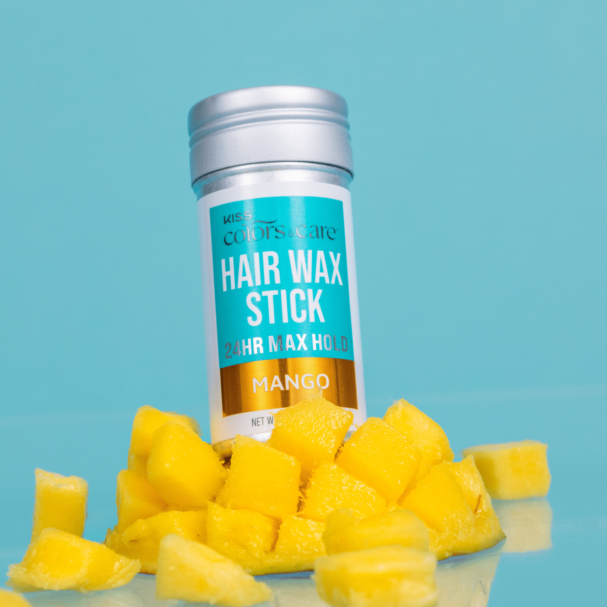 Silver-capped KISS Colors & Care Hair Wax Stick with blue, white, and gold label, surrounded by fresh yellow mango chunks on blue background.
