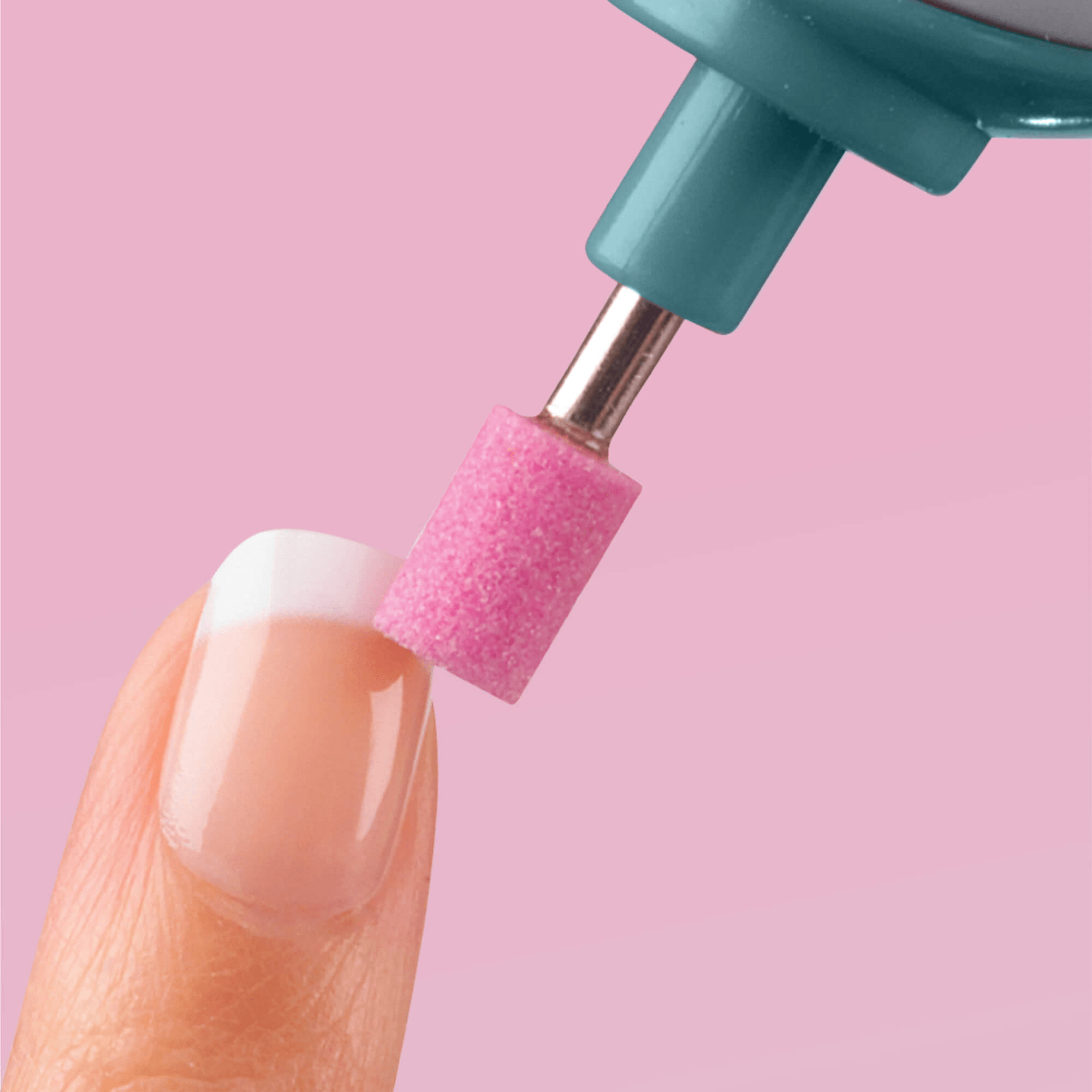 Close-up of a fingernail with a French manicure being filed using a teal KISS Power File X with a pink cylindrical sanding attachment against a pink background.