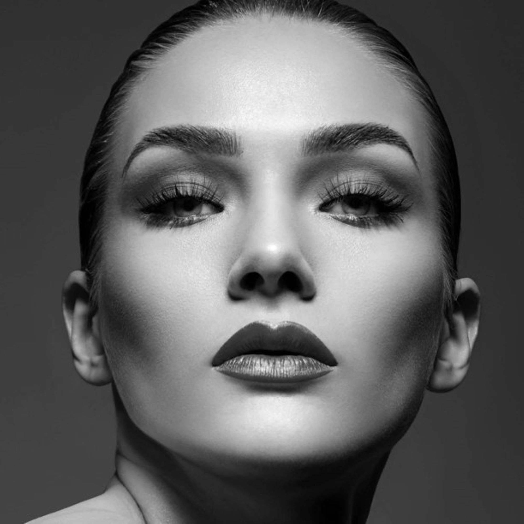Close-up black and white portrait of a woman with smooth skin, bold lips, and voluminous false eyelashes enhancing her eyes.