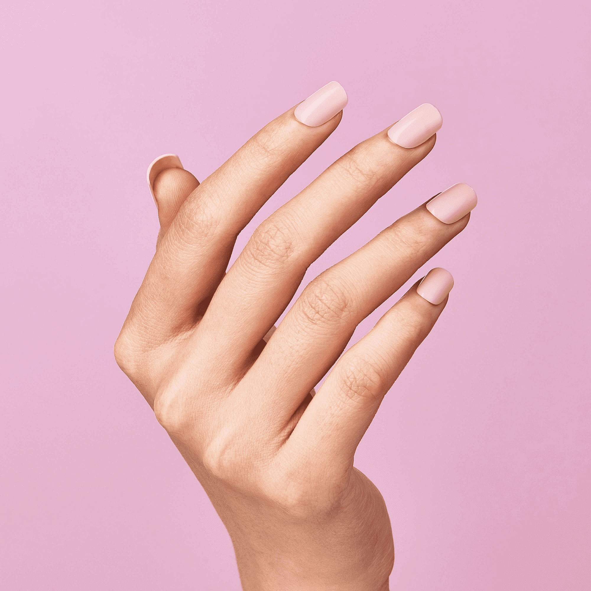 Hand with press-on nails in soft pastel pink color, shown against a matching pink background, highlighting a smooth, glossy finish.