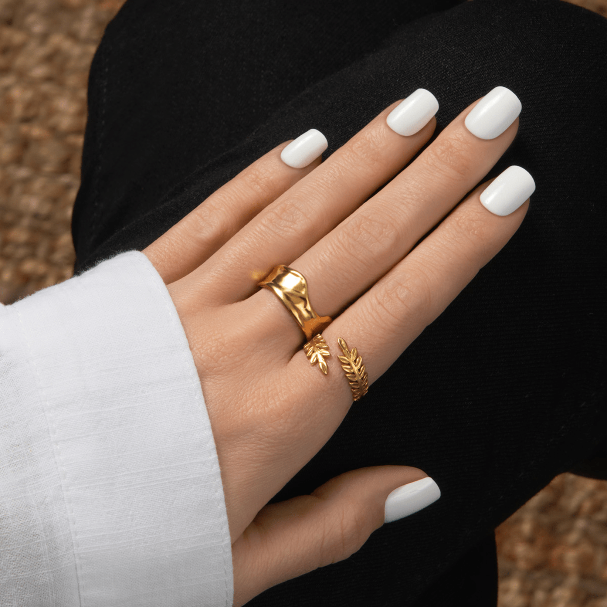 Hand with white nail polish wearing two gold rings against a black background